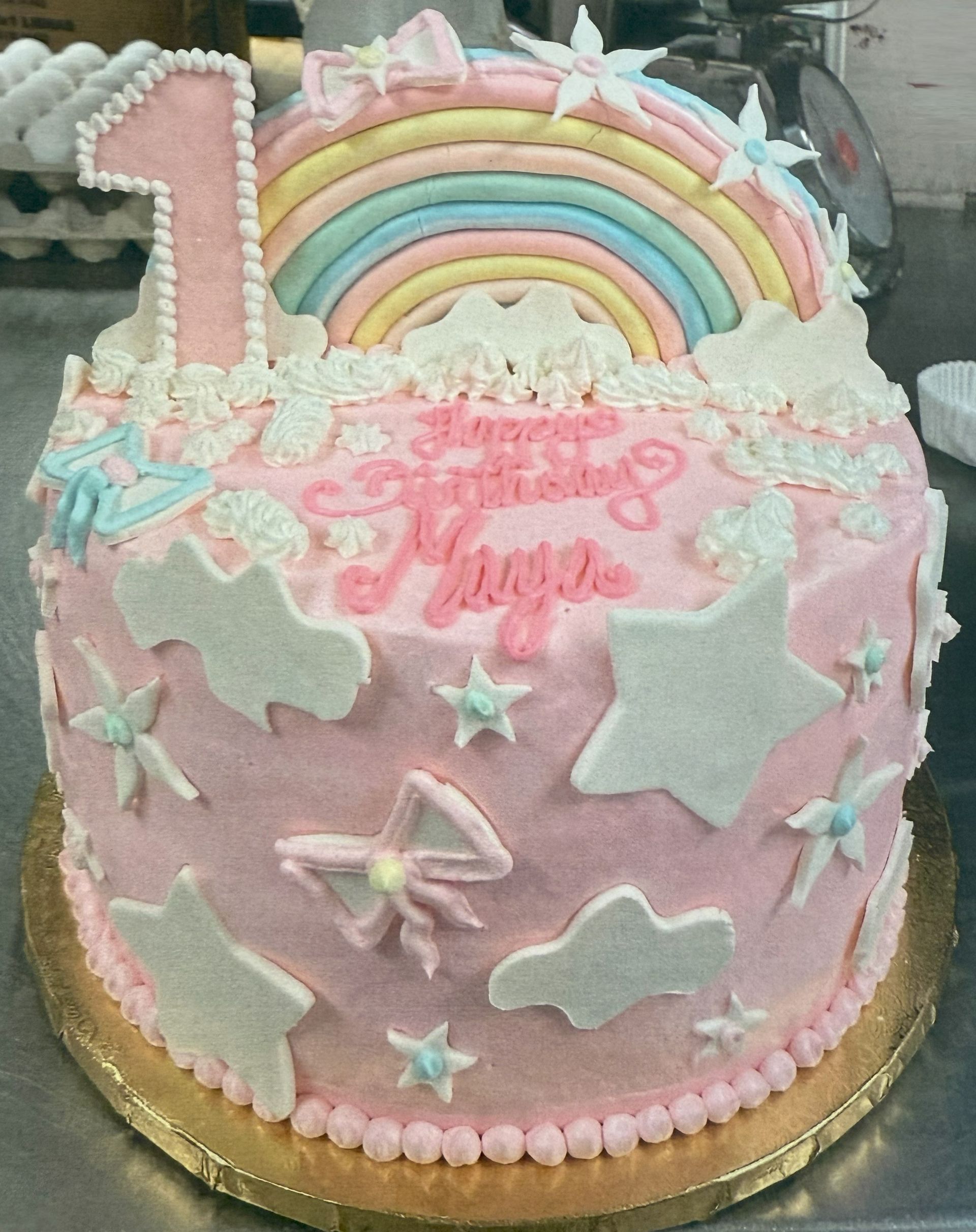 Pink birthday cake with a rainbow, stars, and a number 1, decorated with 