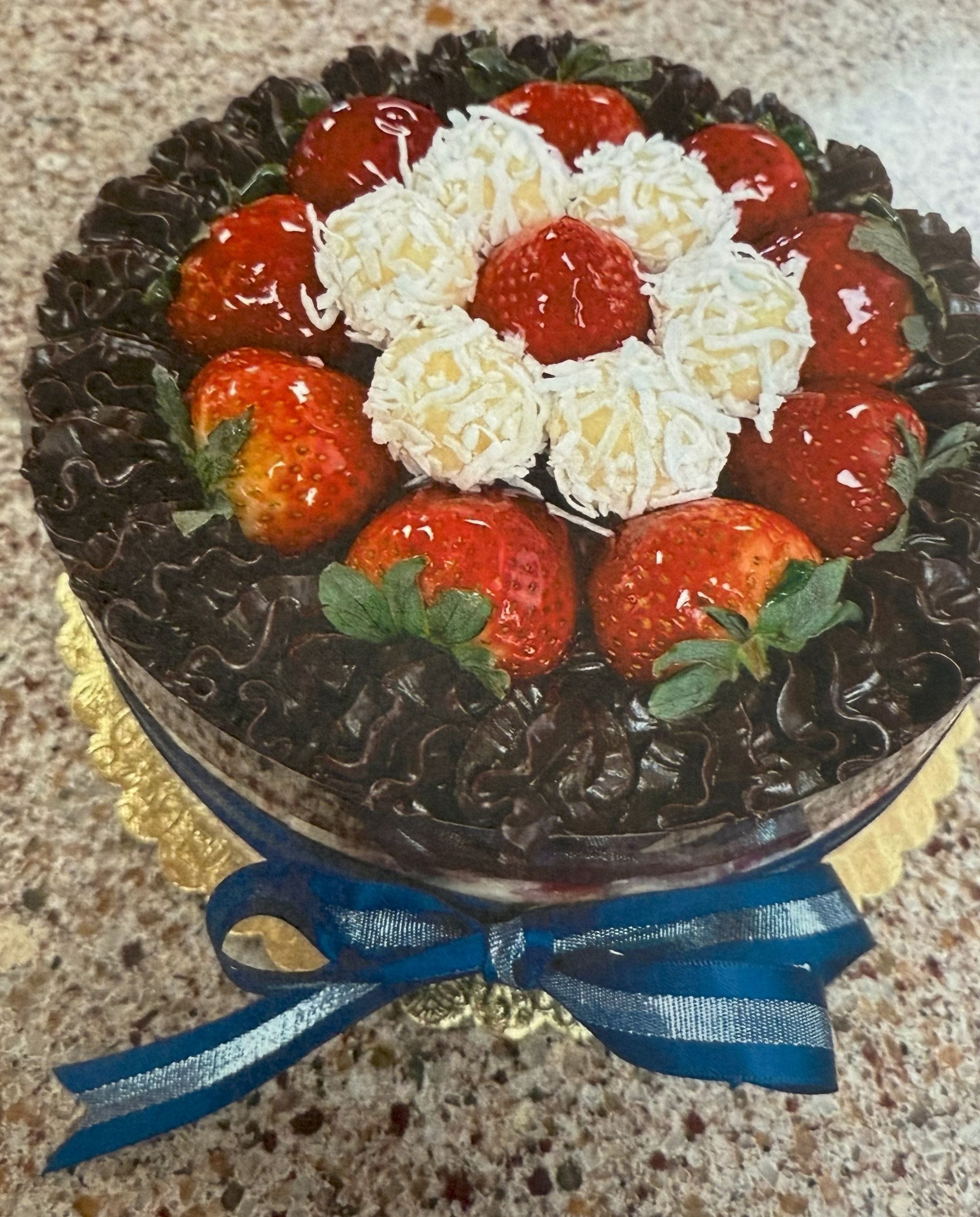 Chocolate cake with strawberries and coconut balls, tied with a blue ribbon.