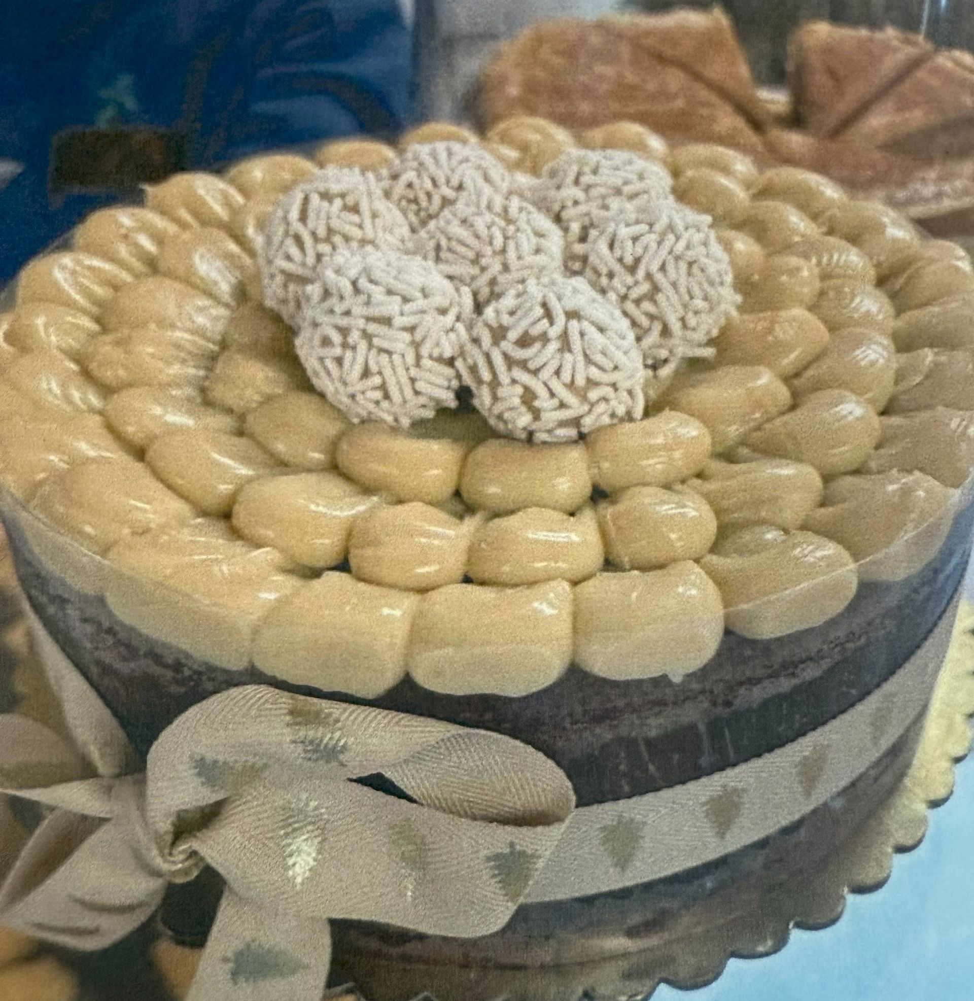 Cake with light brown frosting and white sprinkles, on a decorative ribbon, close-up.