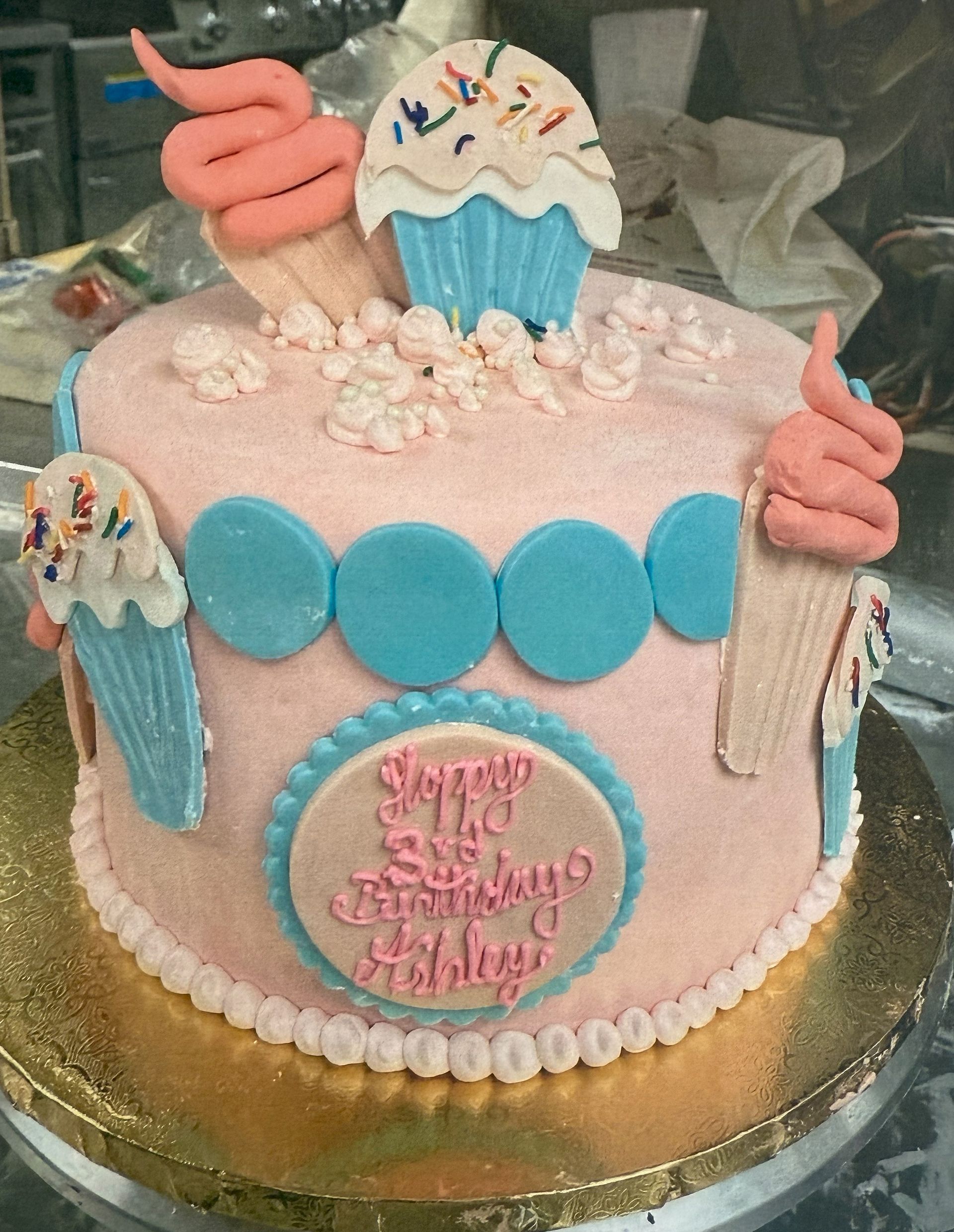 Pink cake decorated with ice cream cones, cupcakes, and a birthday message.