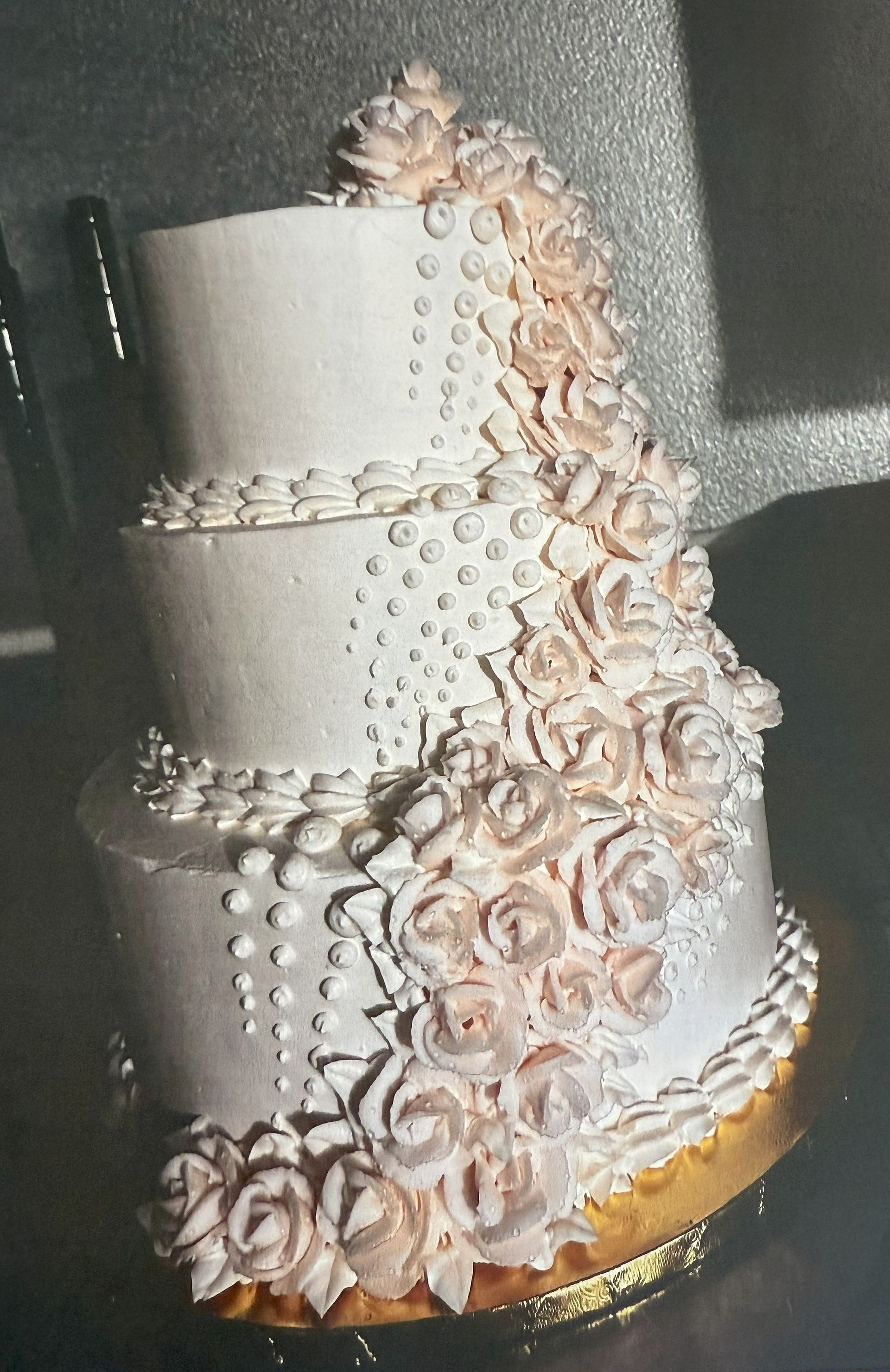 Three-tiered wedding cake with cascading peach-colored frosting roses, pearl accents.