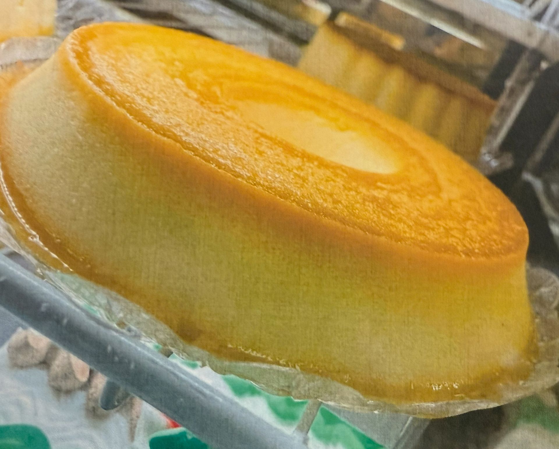 Golden-brown custard cake in a clear container, slightly out of focus, on a shelf.