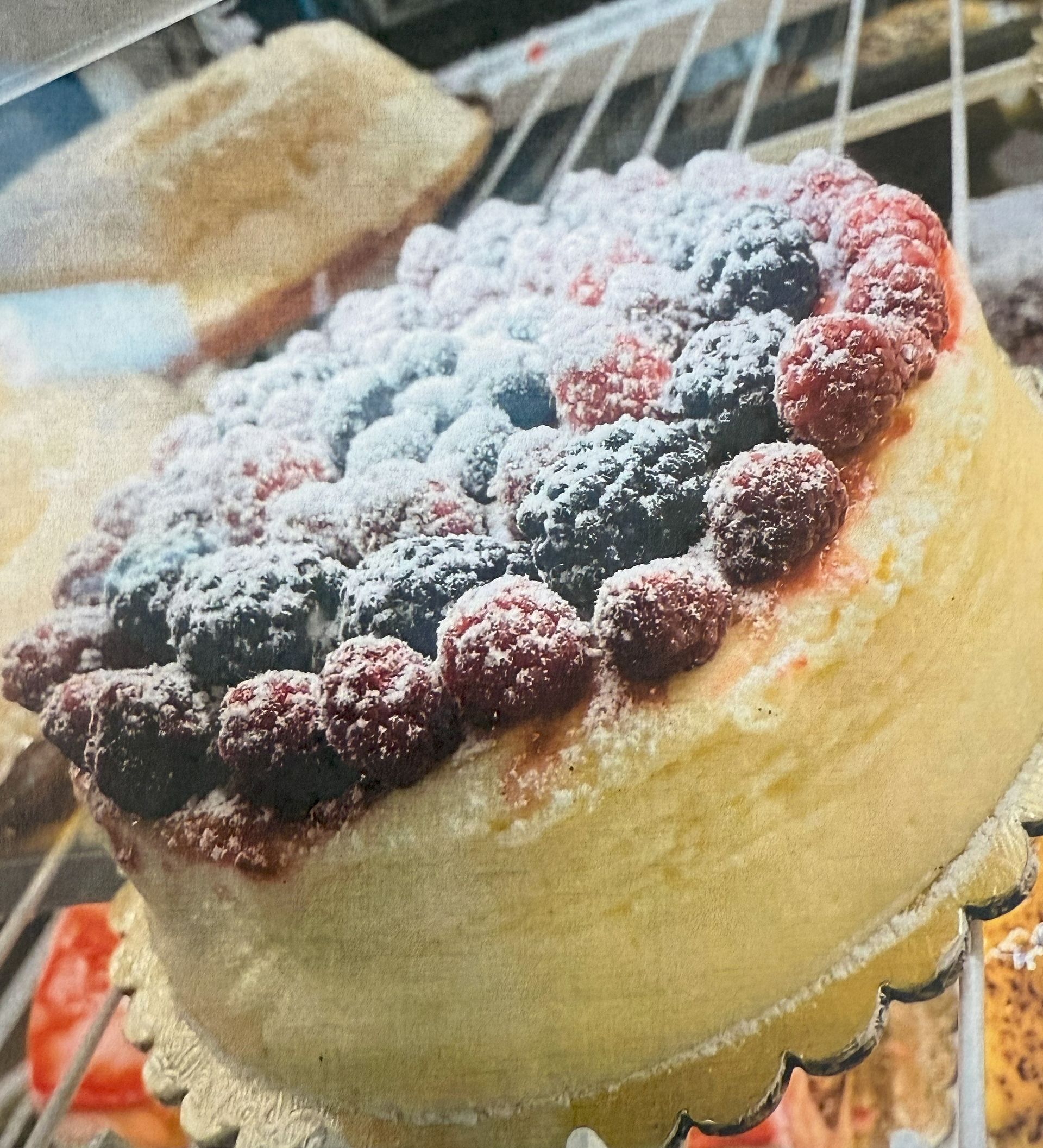 Cheesecake topped with raspberries, blueberries, and blackberries, dusted with powdered sugar, on a gold doily.