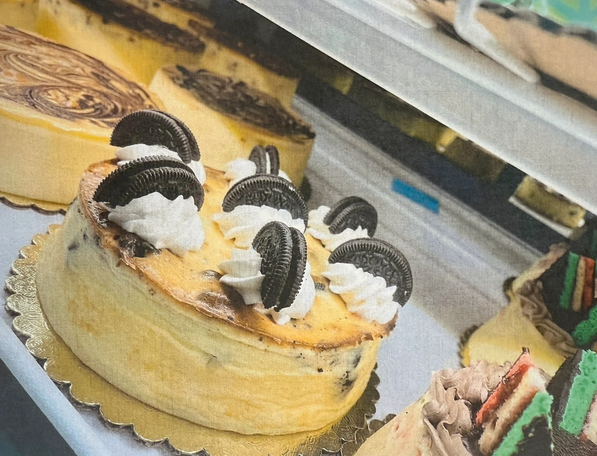 Cheesecake with Oreo cookies and whipped cream, displayed in a bakery case.