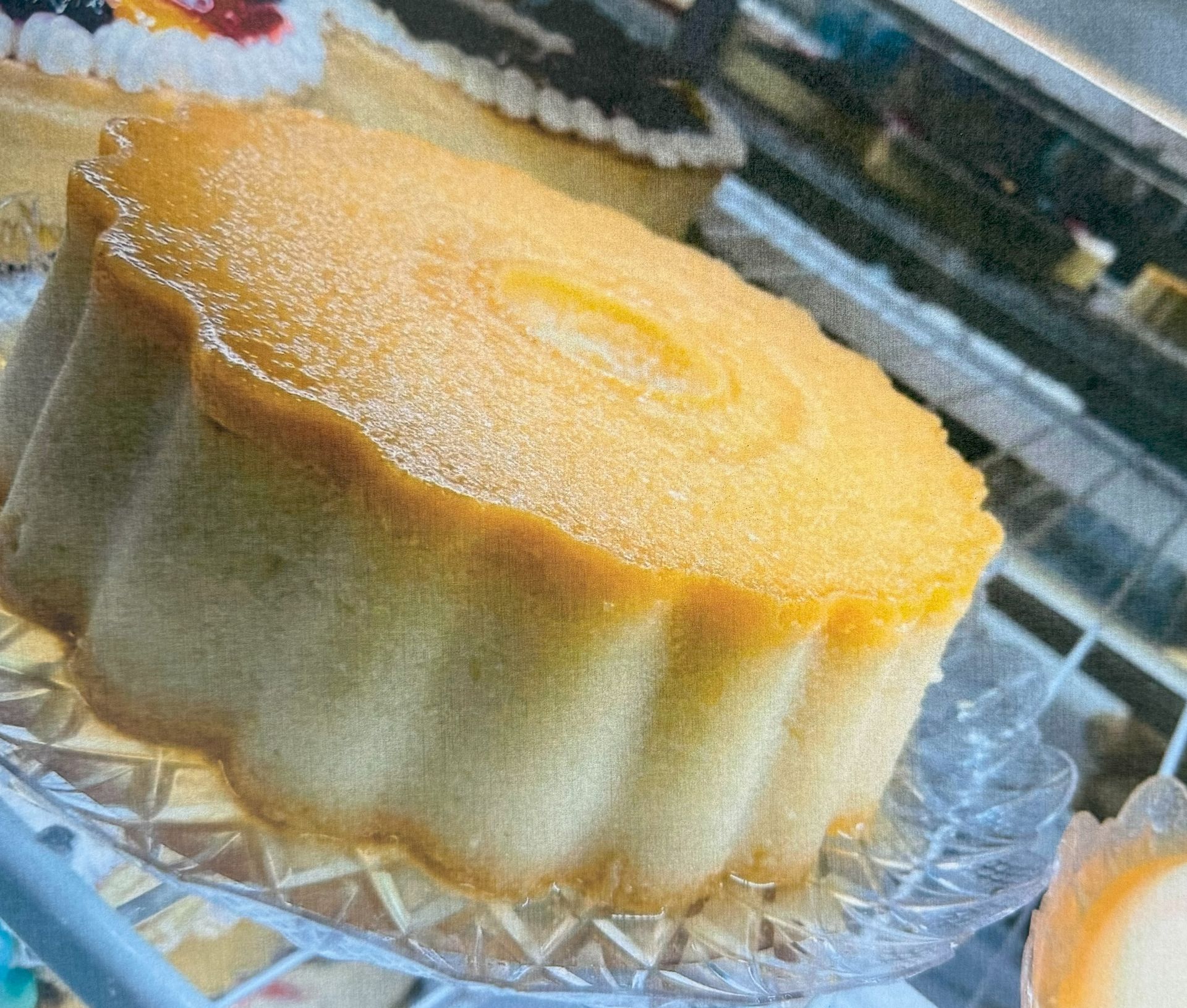 Yellow cake with a scalloped edge, on a glass plate, in a display case.