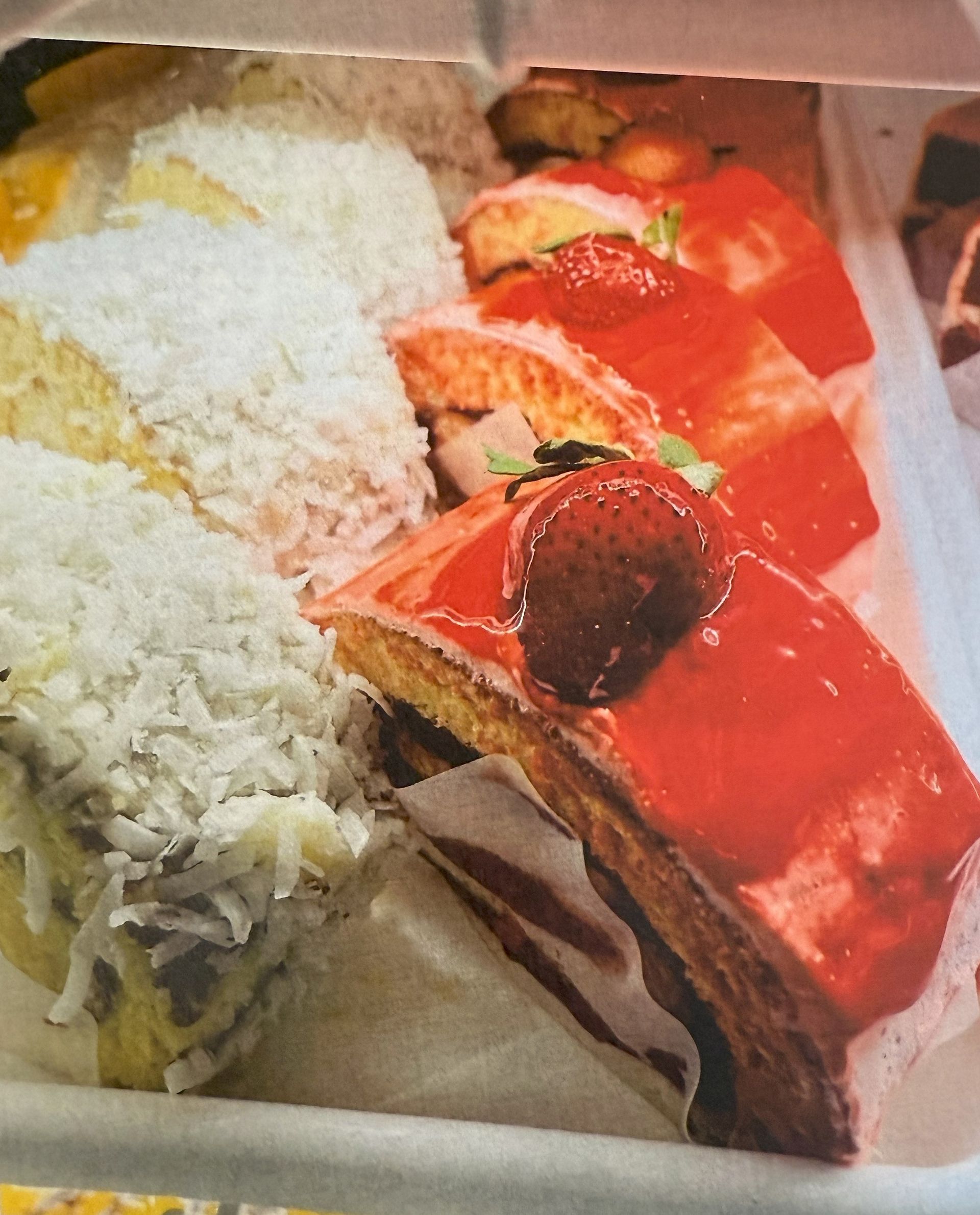 Cakes with coconut and strawberry topping displayed in a bakery case.