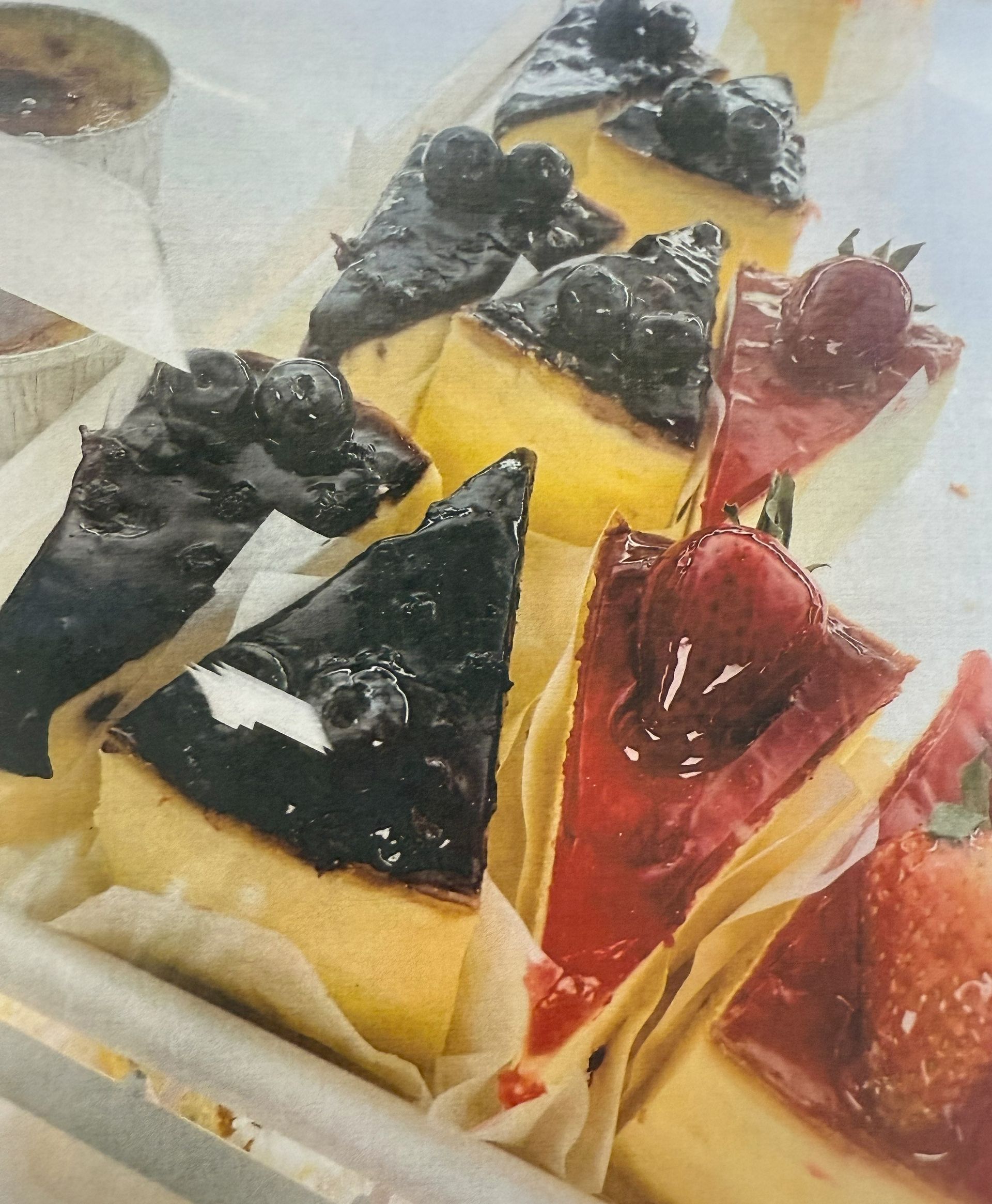 Cheesecake slices with blueberry and strawberry toppings on parchment paper.