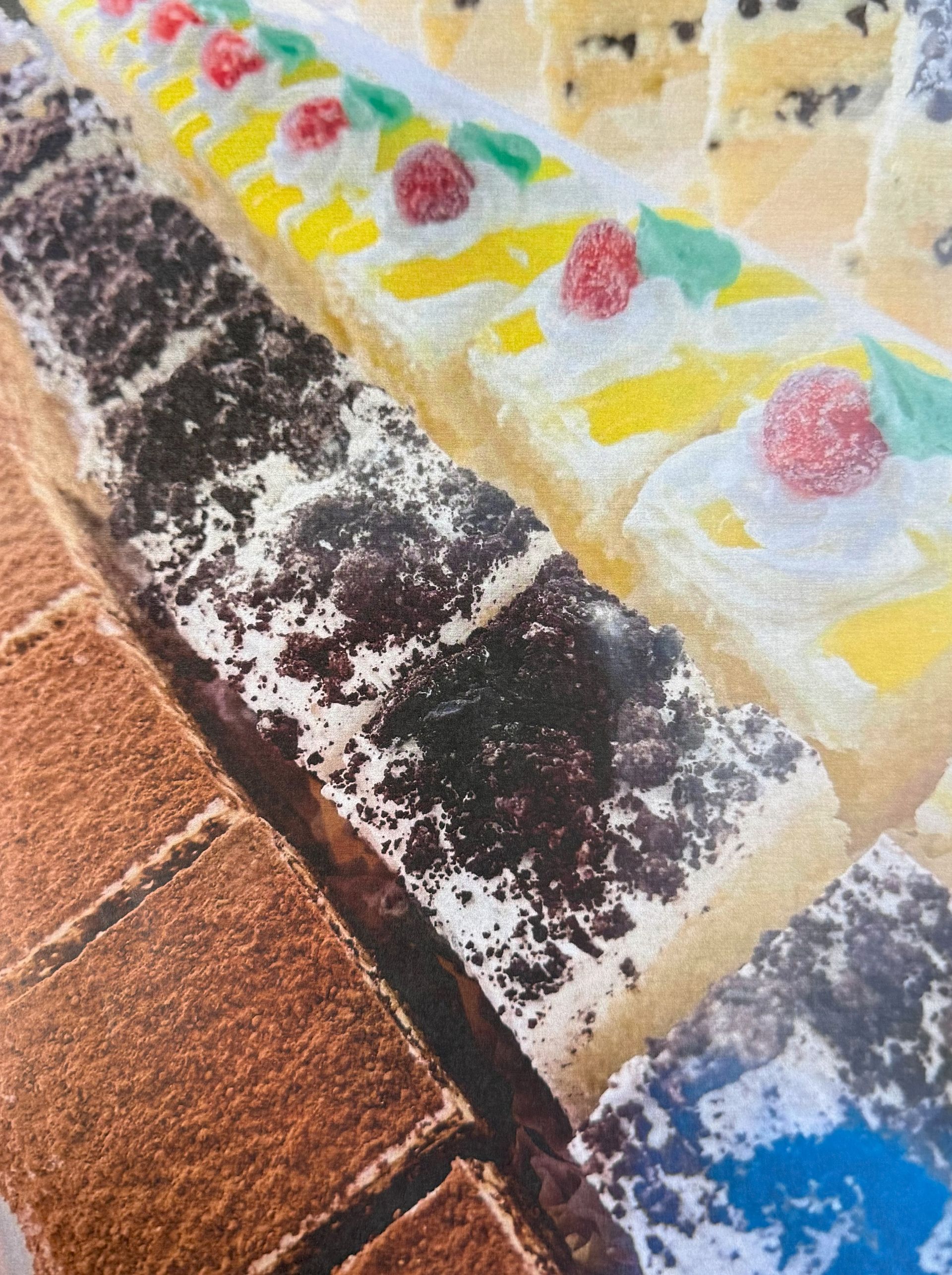 Close-up of various pastries: chocolate-covered, yellow with whipped cream, and rows of small square ones.