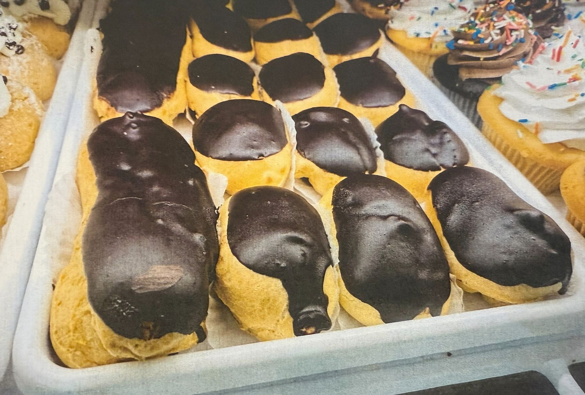Tray of chocolate eclairs in a bakery display case.