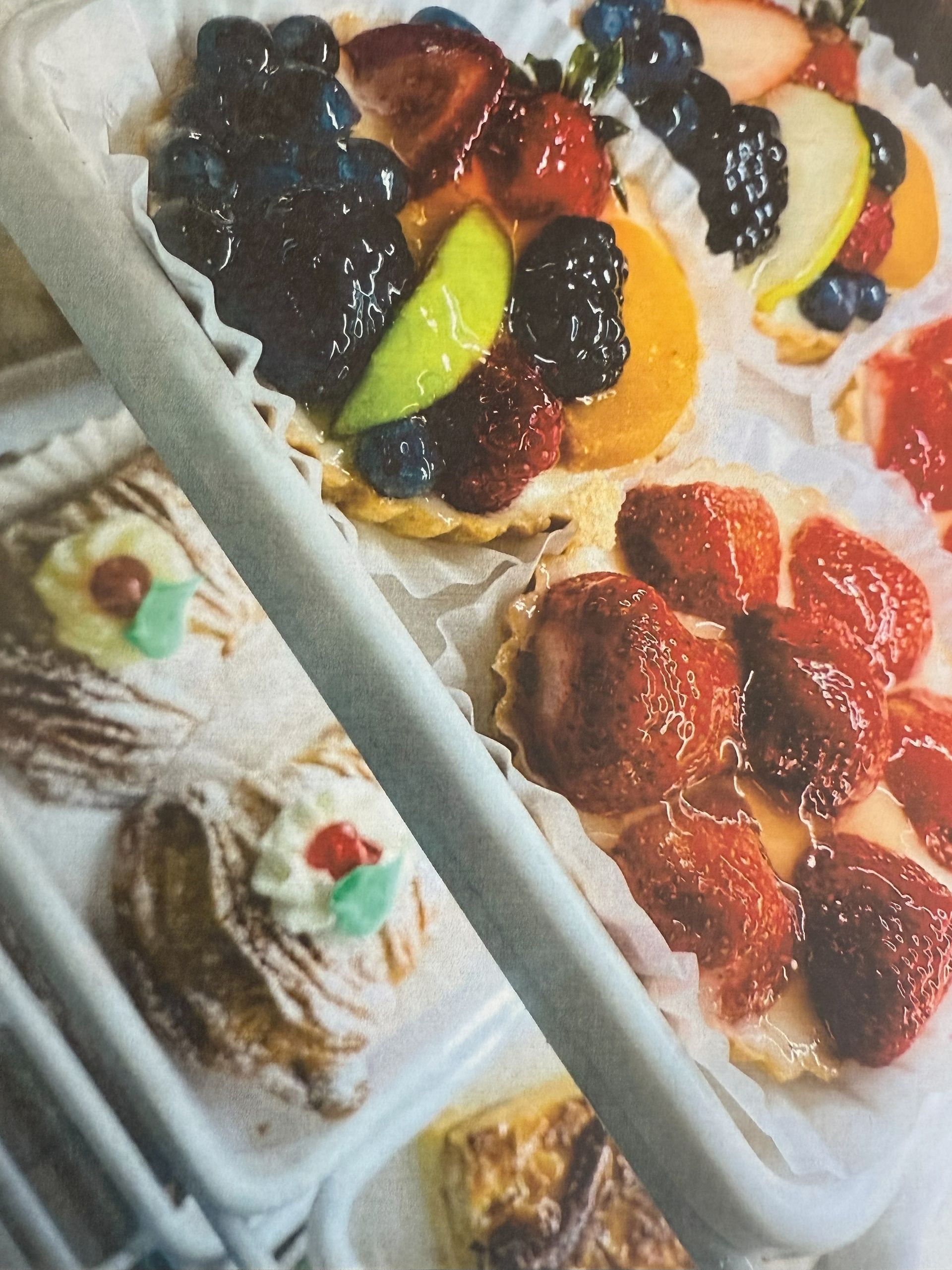 Pastries: fruit tarts with berries and slices, plus a cream-topped pastry on display.
