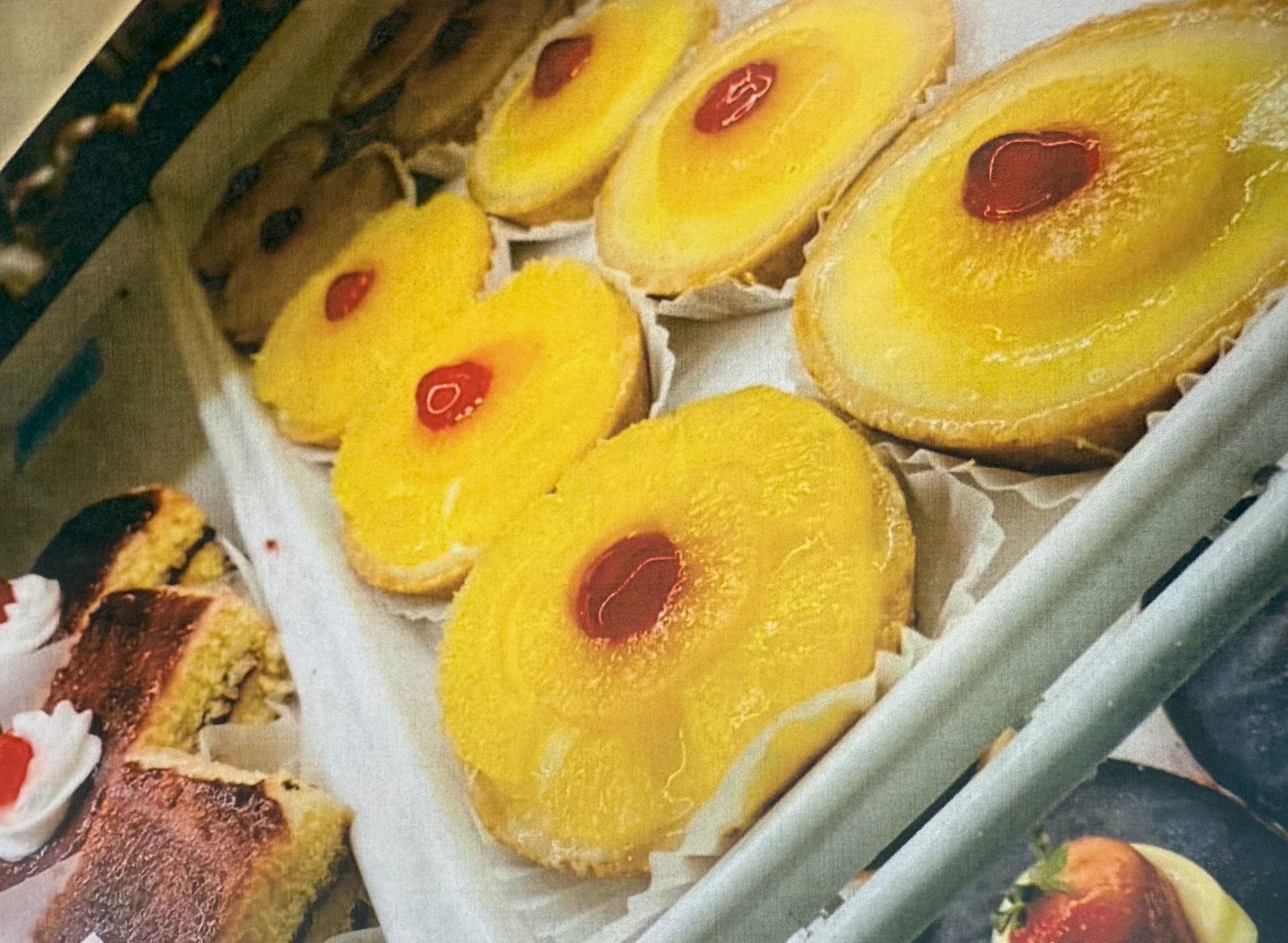 Pineapple pastries with red cherries on display in a bakery.