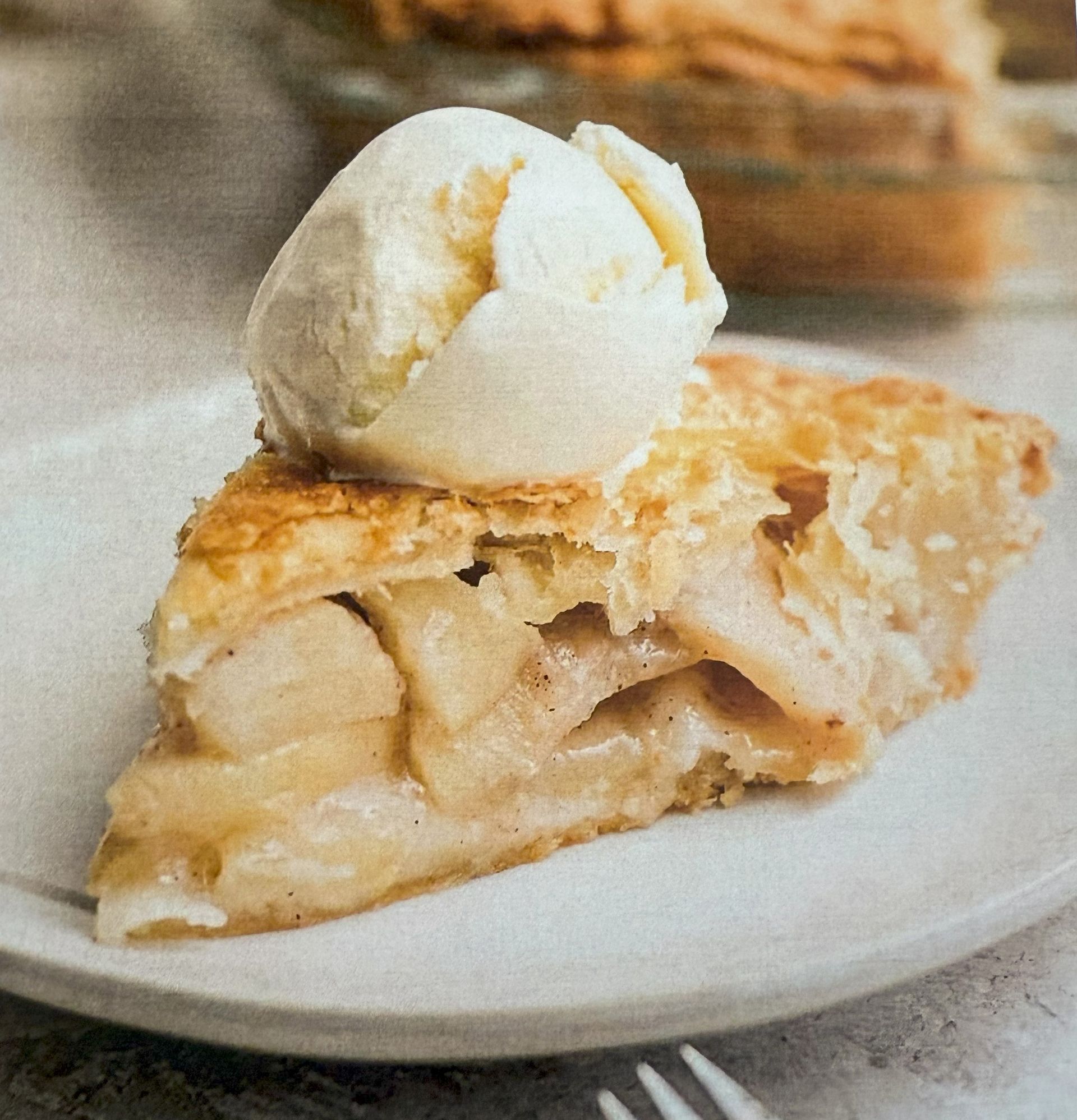 Slice of apple pie topped with vanilla ice cream on a white plate.