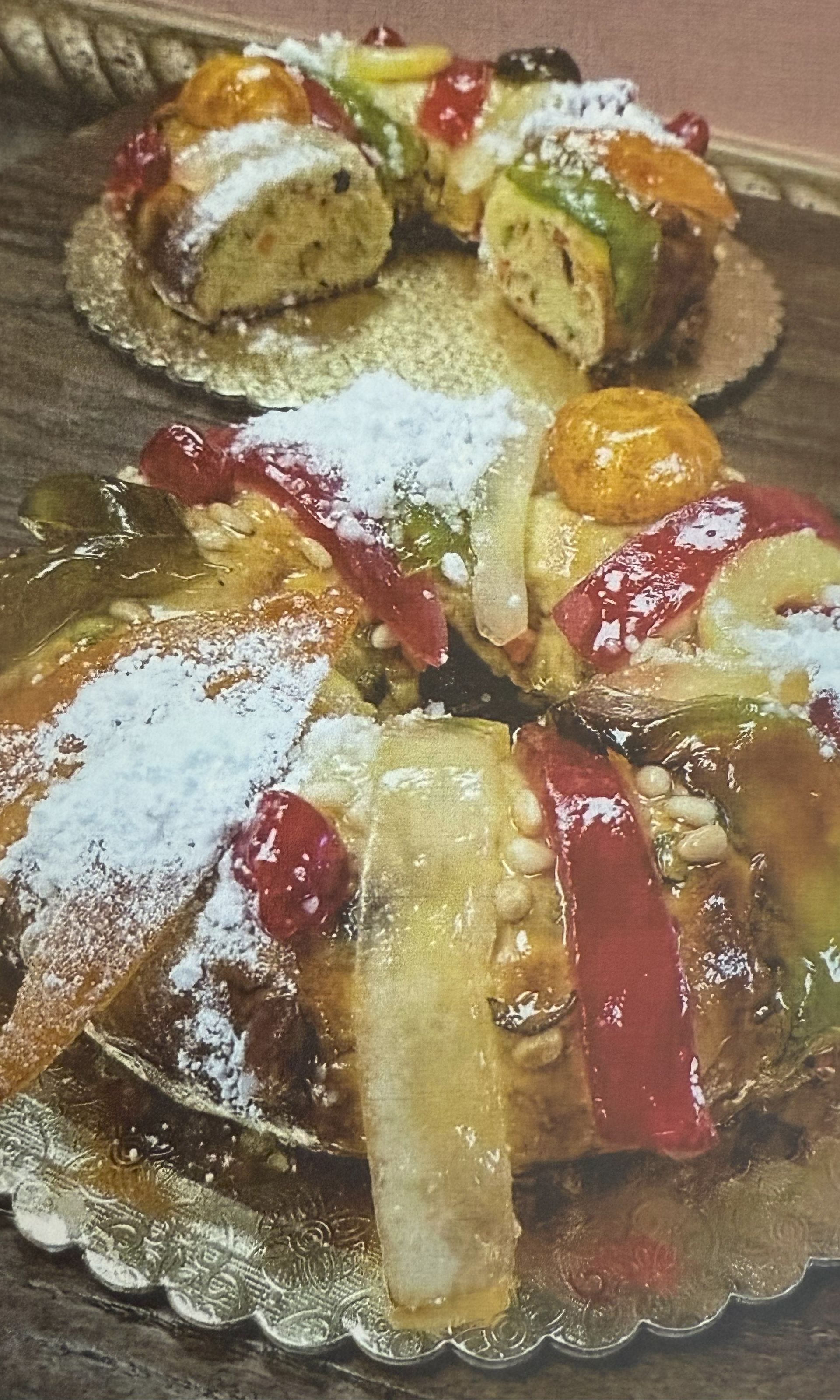 Two ring-shaped cakes with candied fruit and powdered sugar on gold plates, one partially sliced.