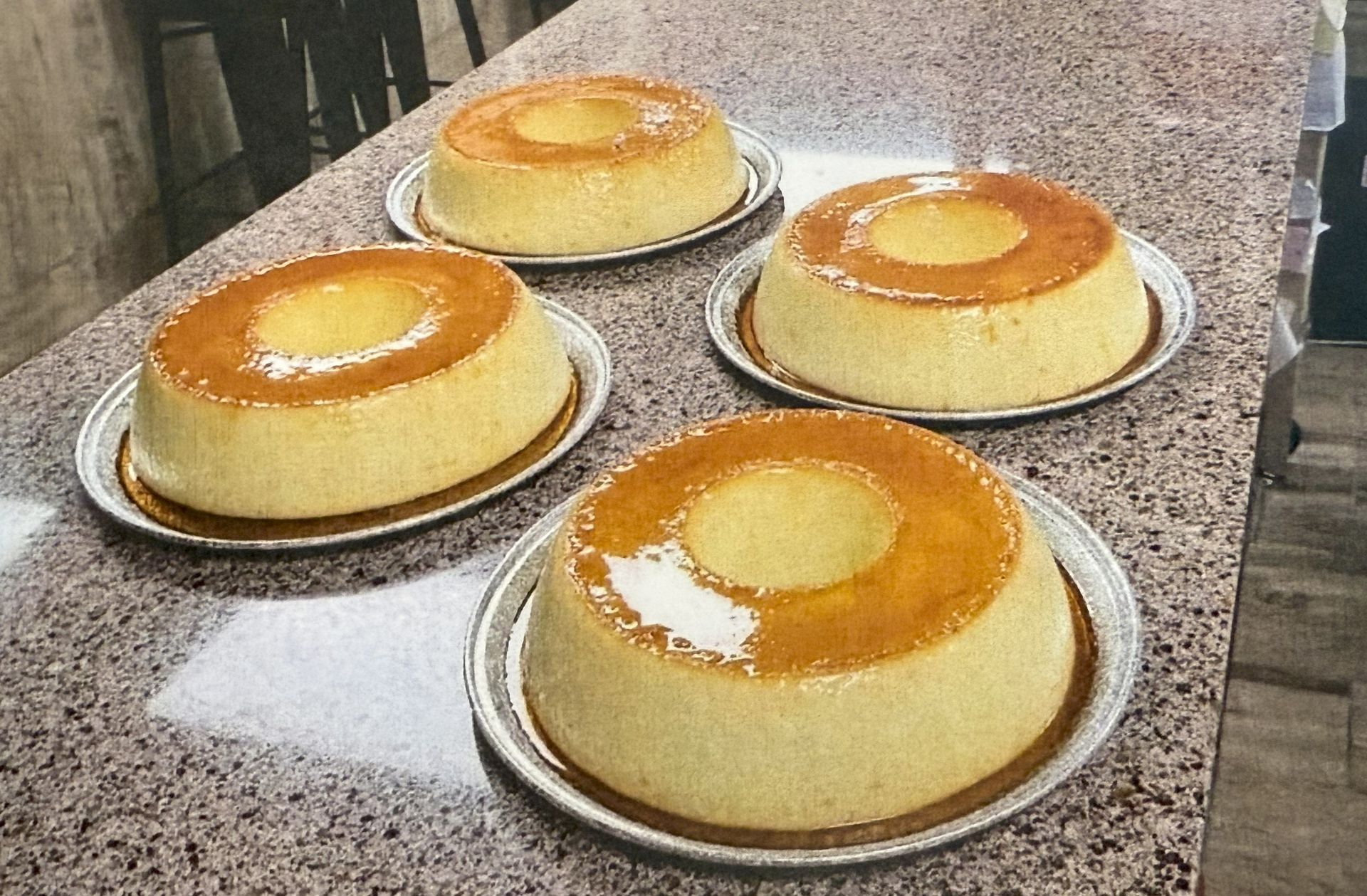 Four flan desserts with a caramel glaze on silver plates.