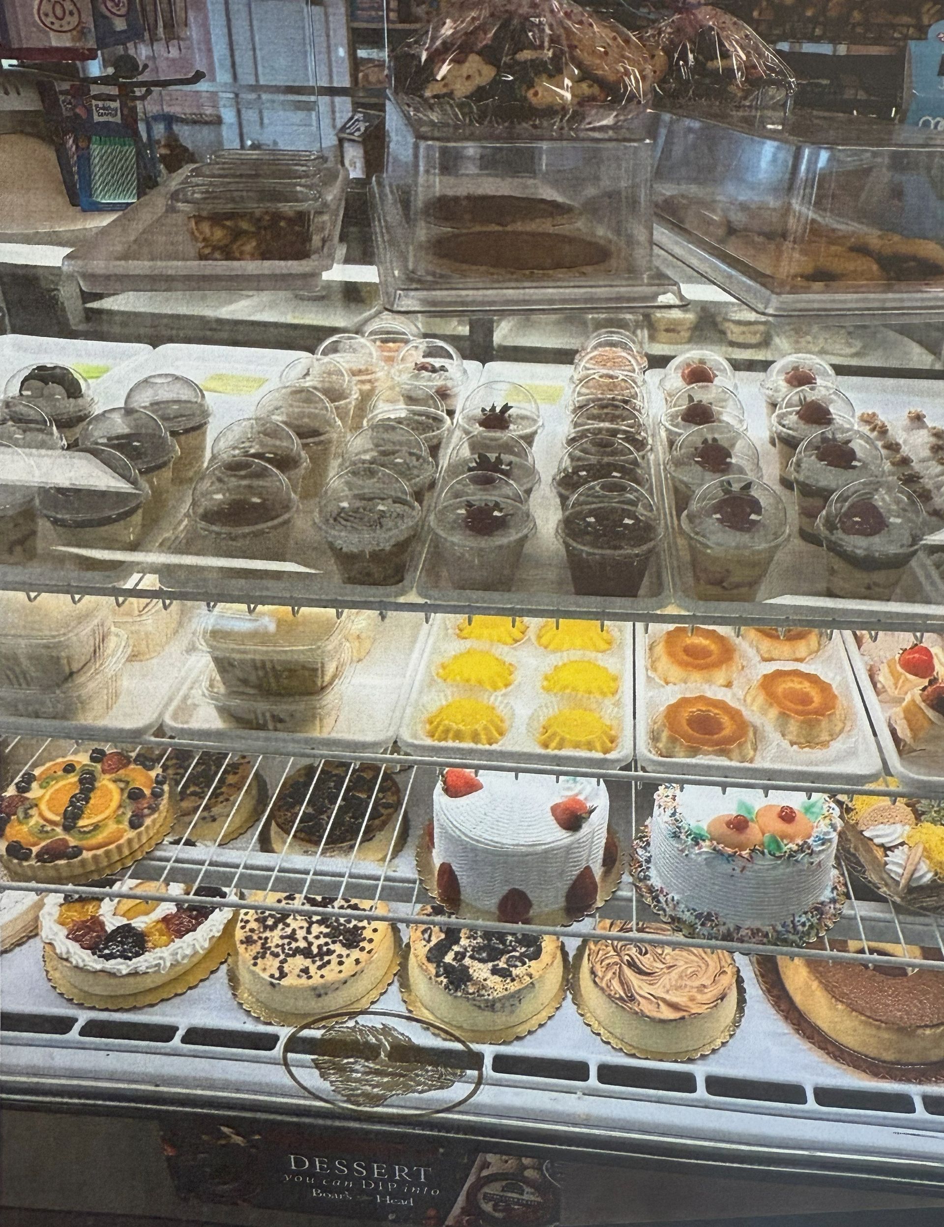 Bakery display case filled with cakes, cupcakes, and pastries; white and clear packaging.