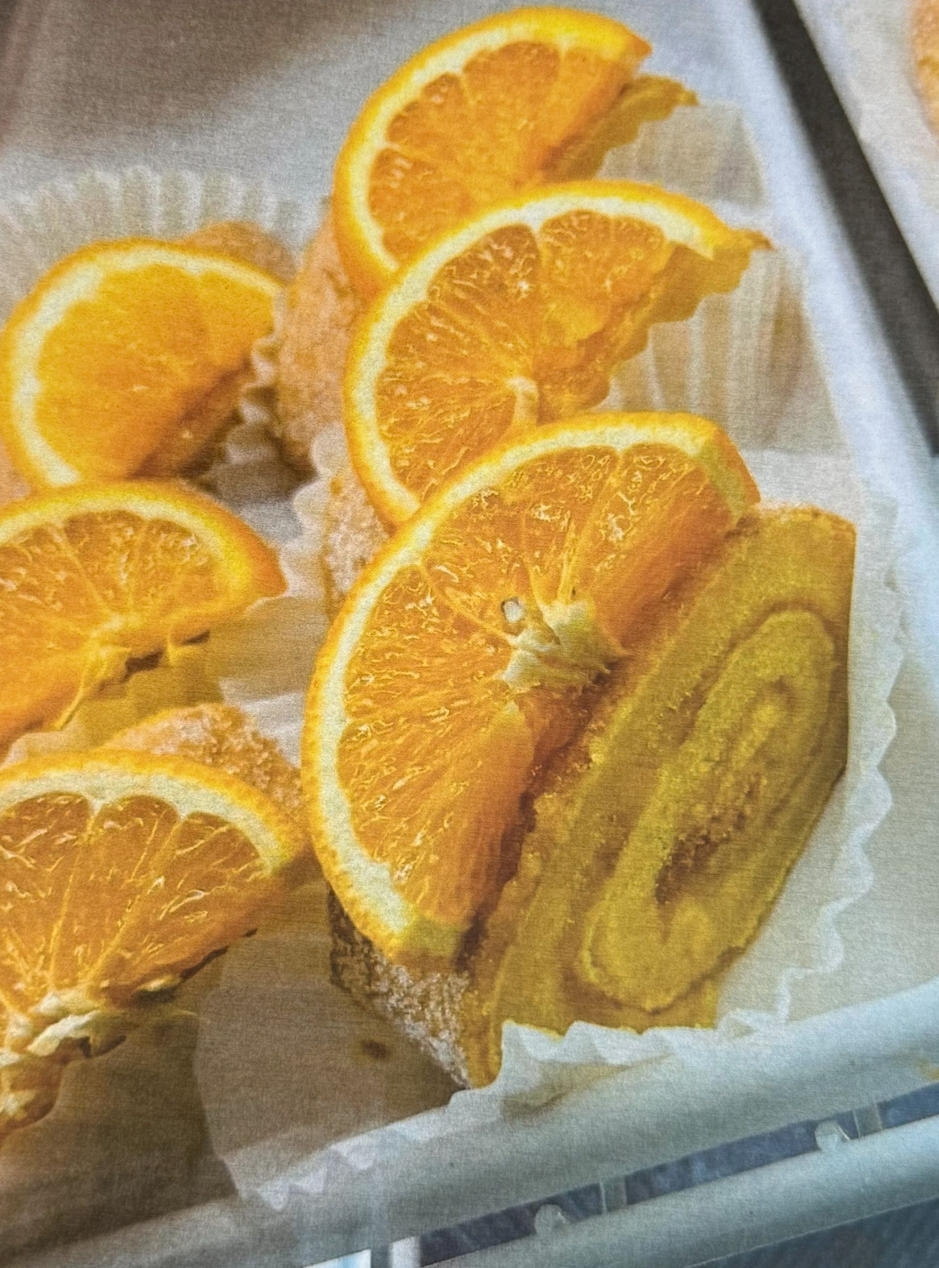 Orange-flavored pastries topped with orange slices in white paper cups.