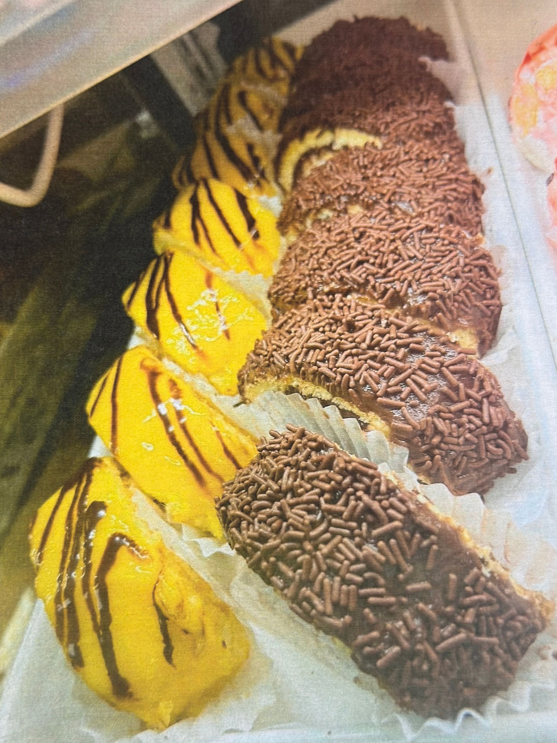 Eclairs with yellow and chocolate frosting, displayed in a bakery case.