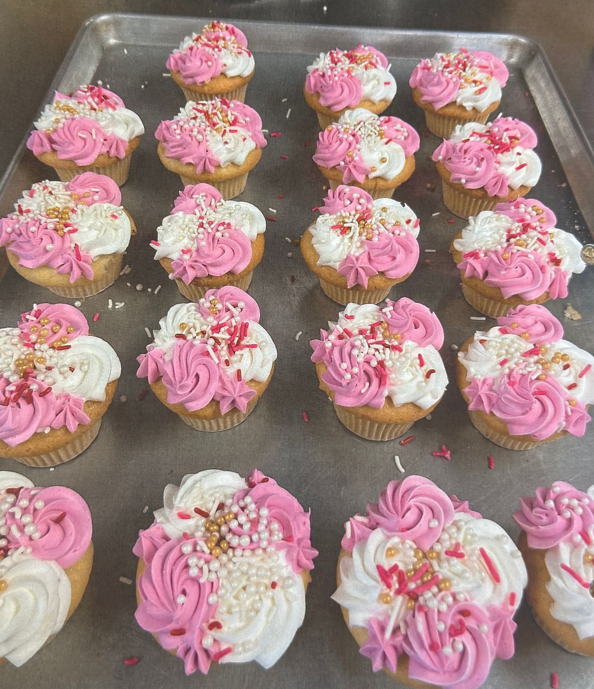 Cupcakes on a tray: pink and white frosting, sprinkles.