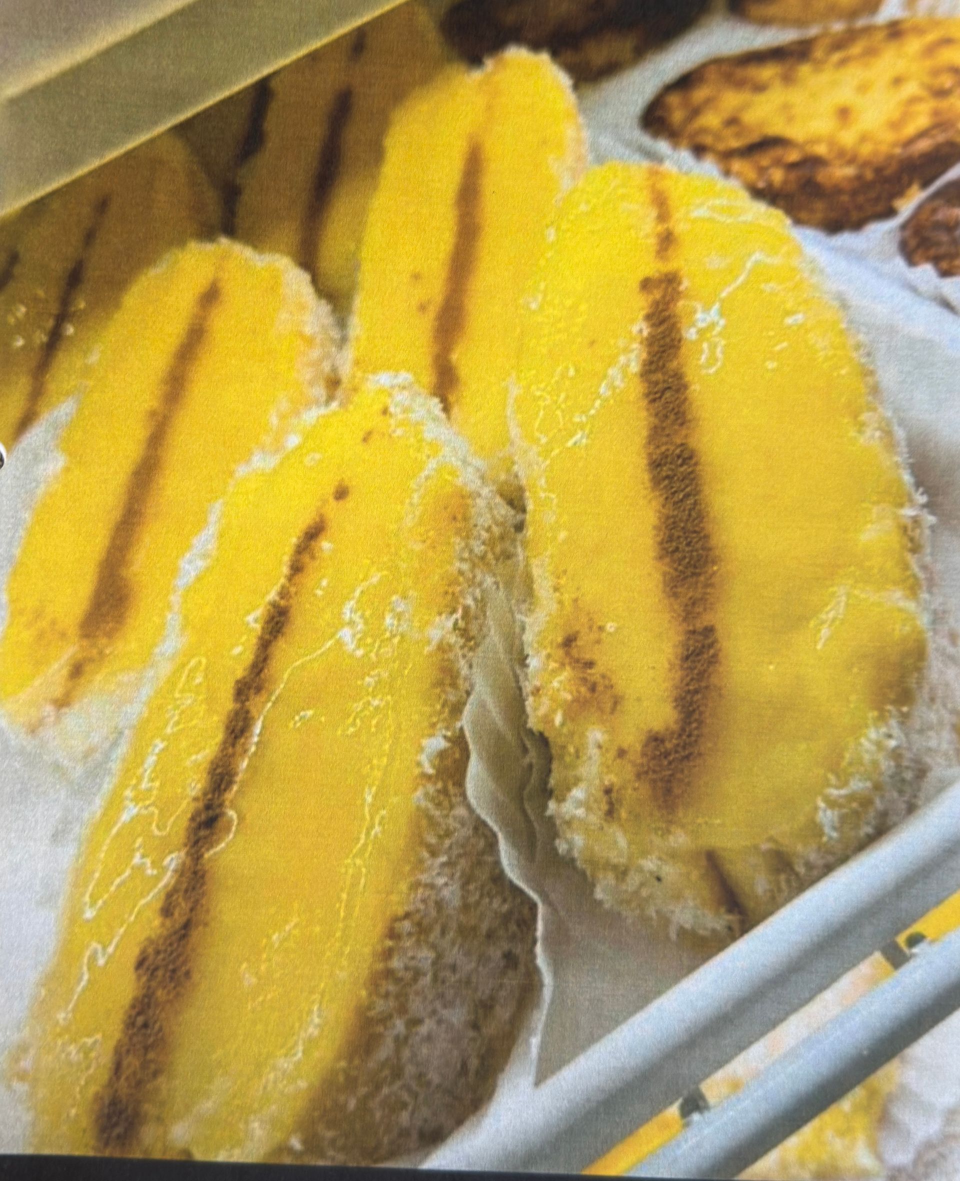 Yellow, sugar-coated fried bananas with brown stripes on display at a bakery.
