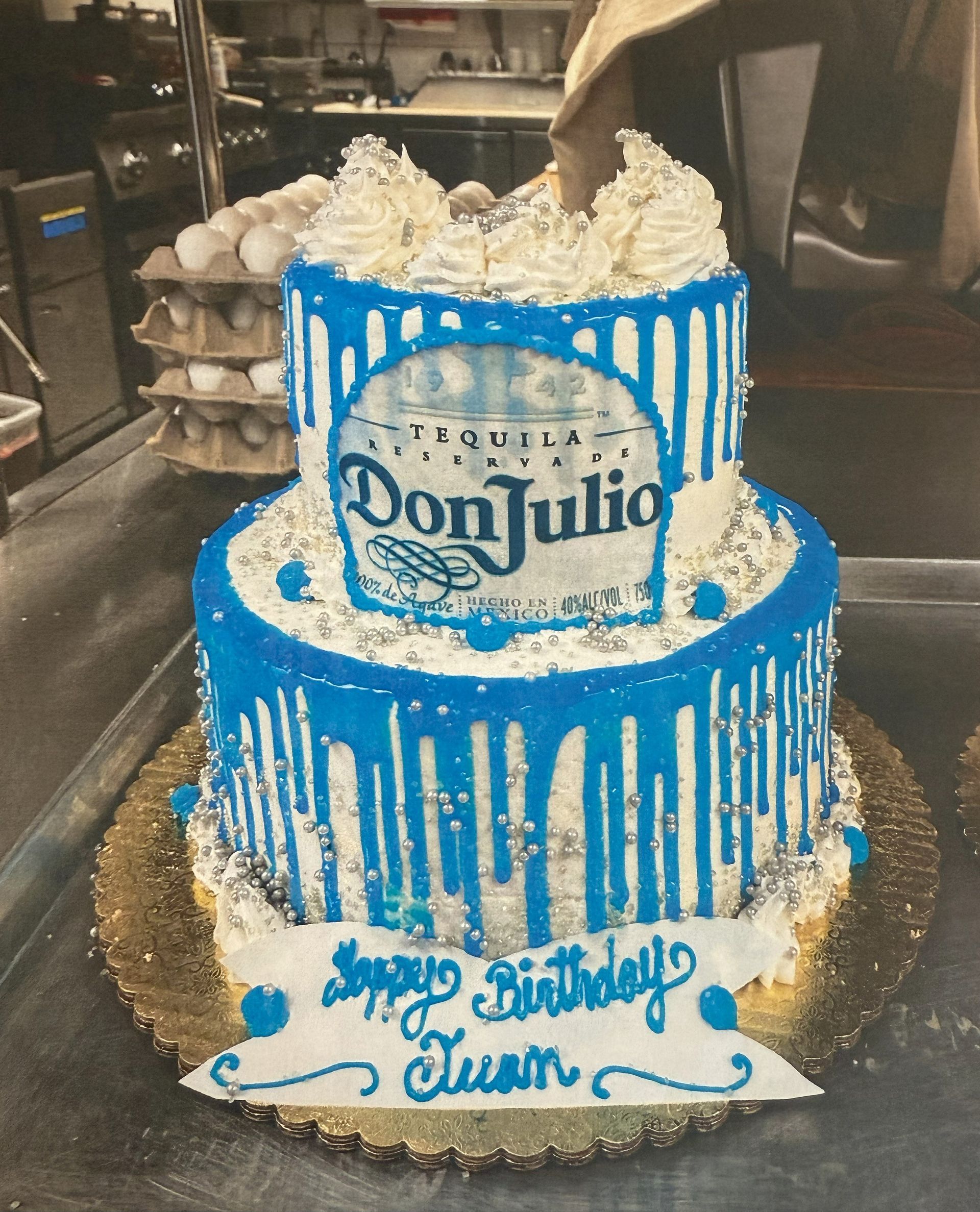 Two-tiered cake with blue frosting, Don Julio logo, white drips, and 
