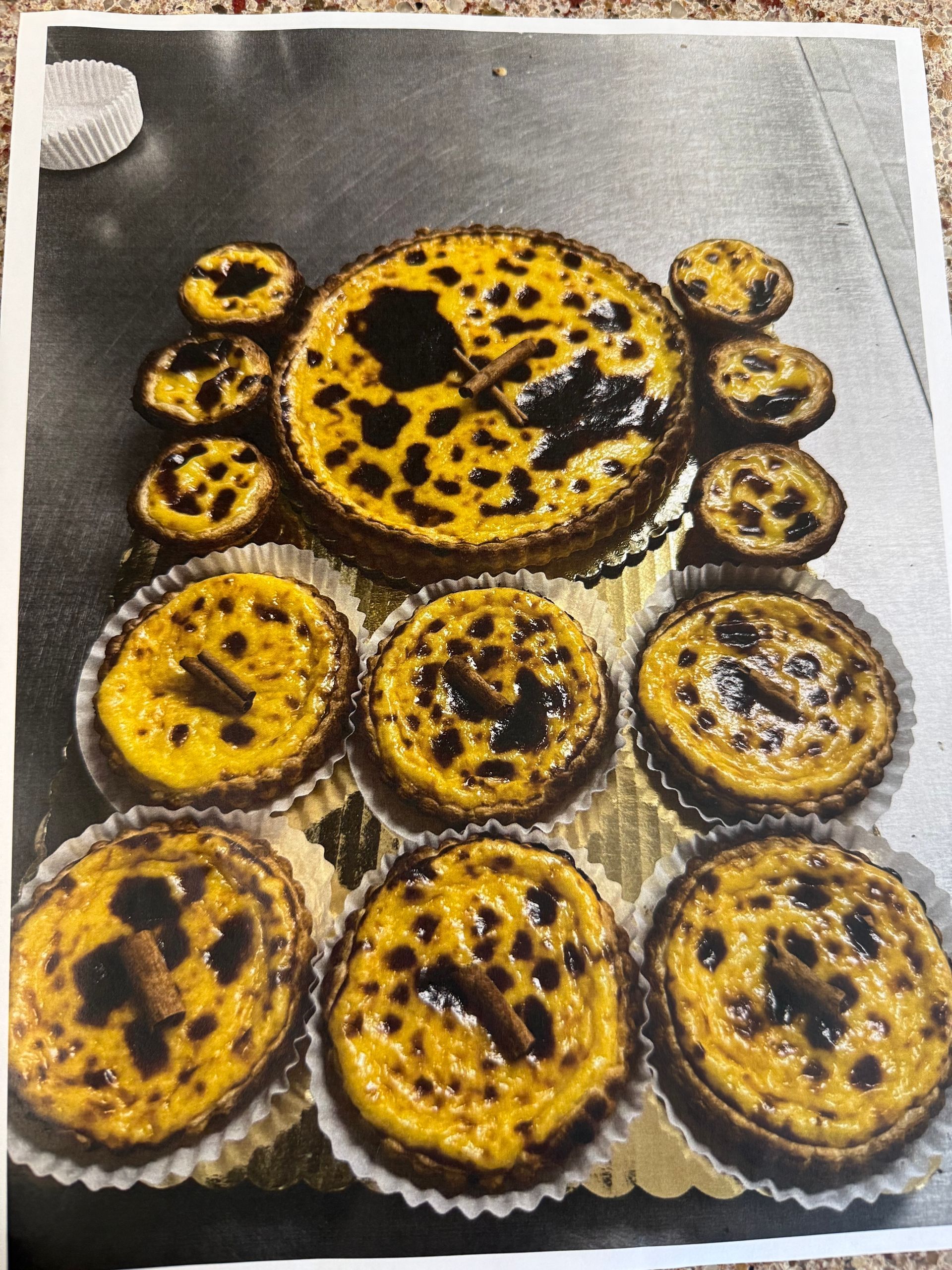 Arrangement of various sized Portuguese custard tarts, with dark caramelized tops, on a golden surface.