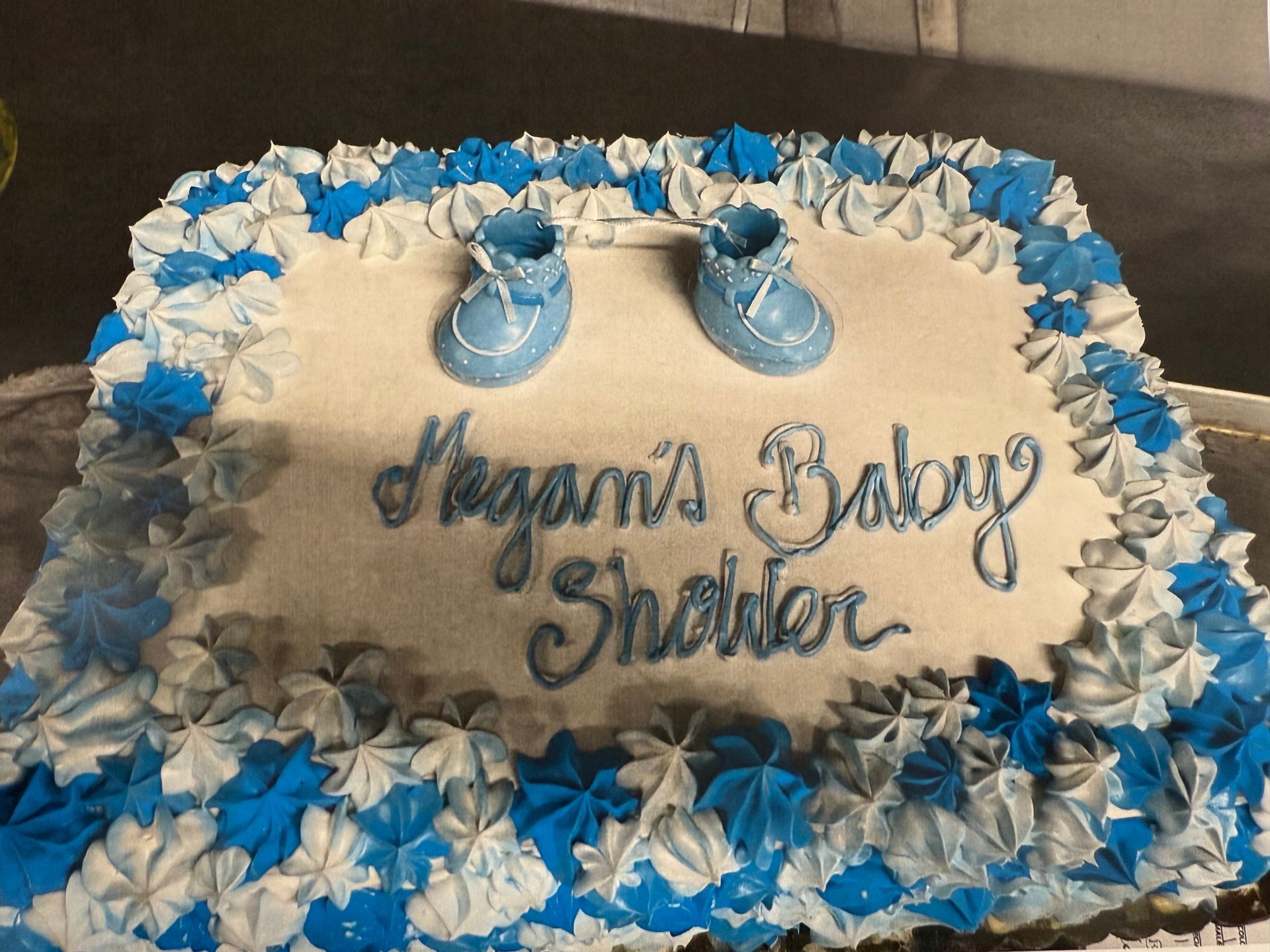 Baby shower cake for Megan, white frosting with blue and white star-shaped borders and lettering, blue baby shoe decorations.