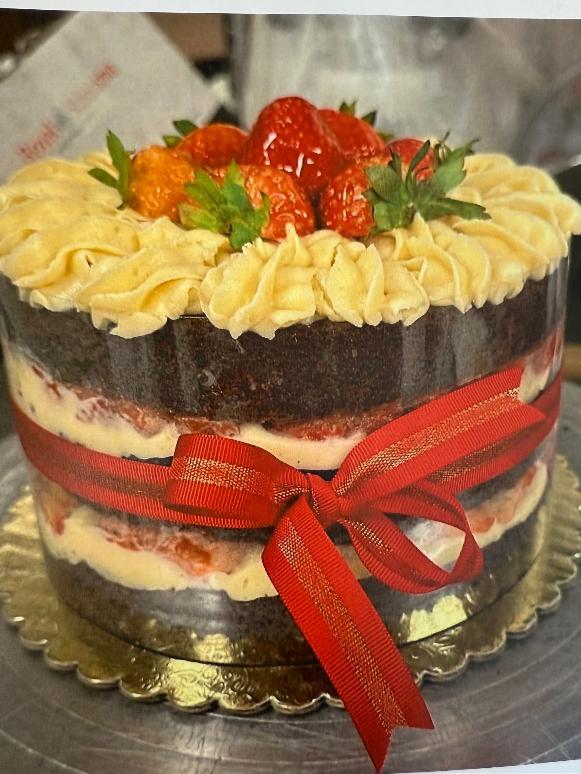 Chocolate cake with cream frosting, strawberries, and a red ribbon.