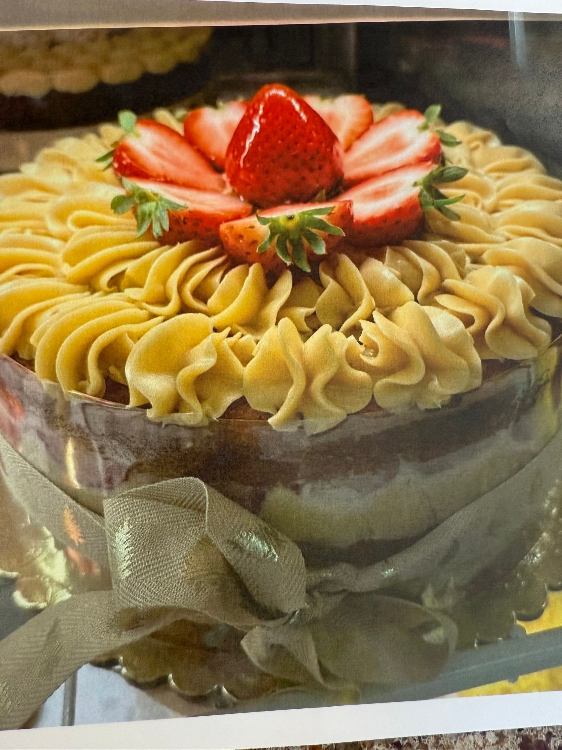 Cake with tan frosting, strawberries, and gold ribbon.