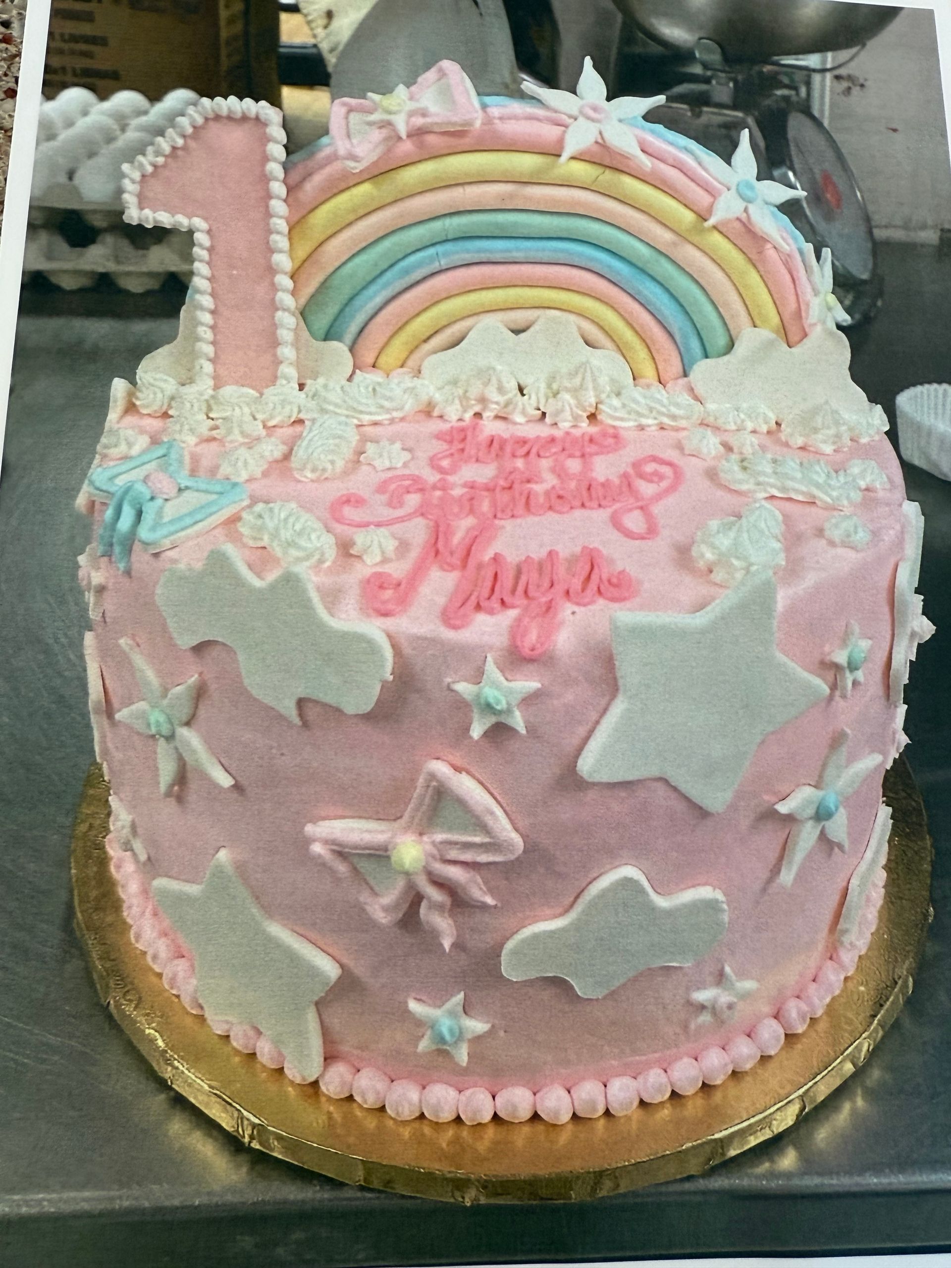 Pink birthday cake decorated with a rainbow, clouds, stars, and 