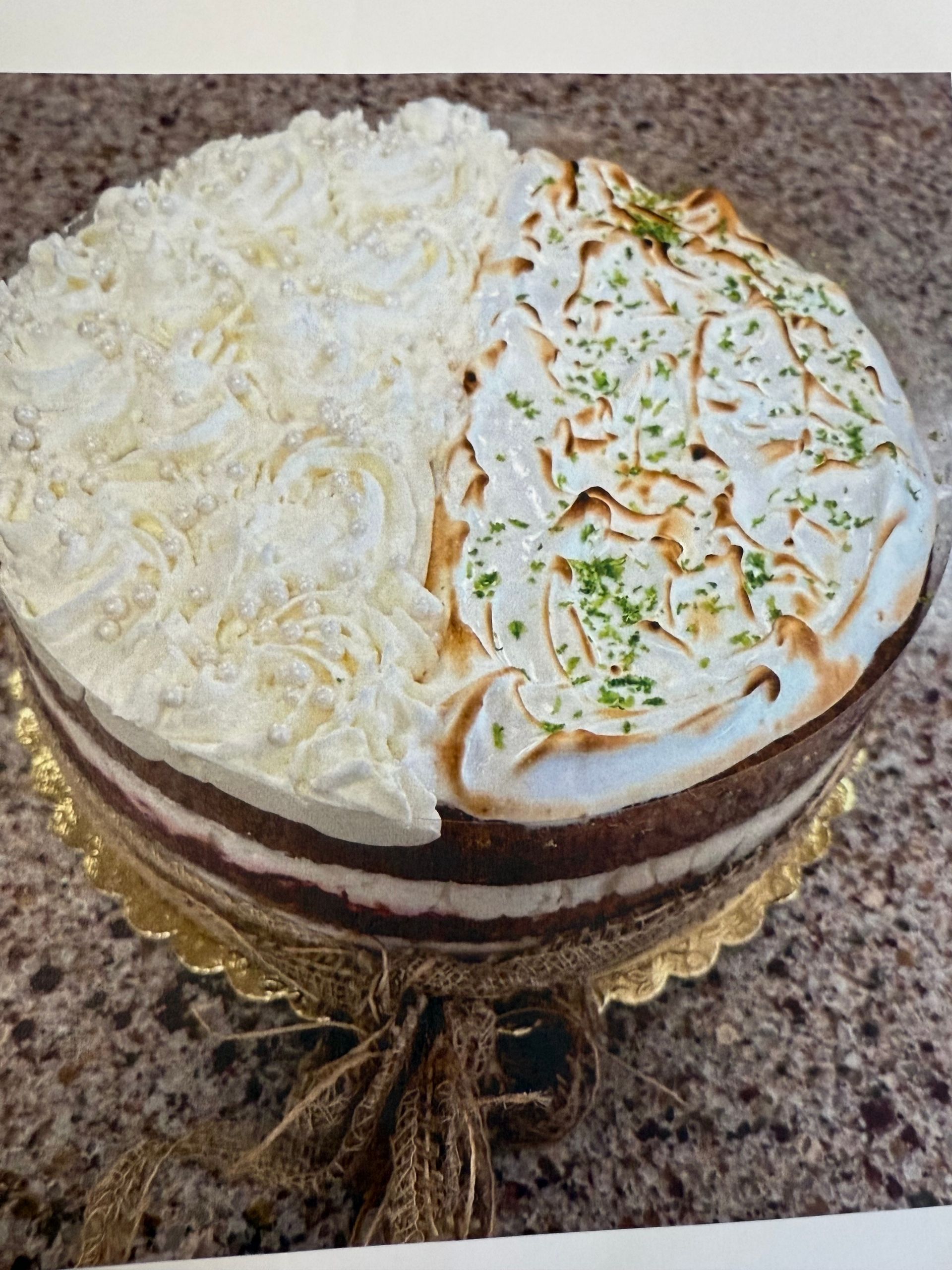 Two-toned cake with white frosting on one half, torched meringue and lime zest on the other, on a gold scalloped plate.