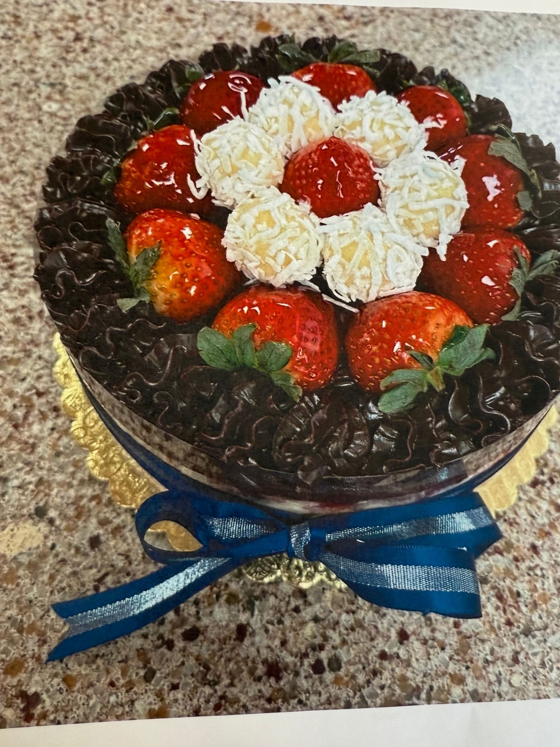 Chocolate cake with strawberries and white coconut balls, tied with a blue ribbon.