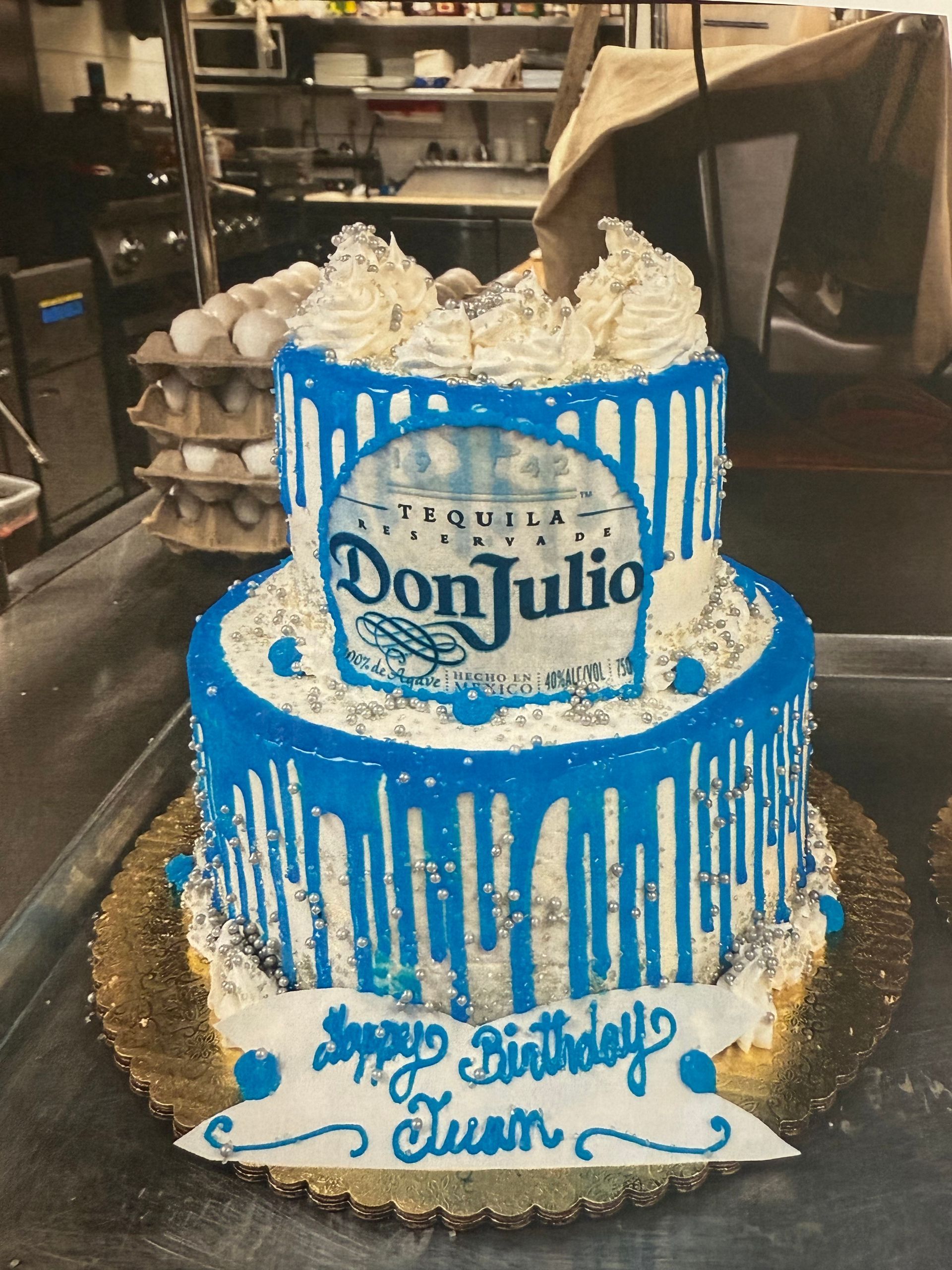 Two-tiered Don Julio birthday cake with blue drip, white frosting, and 