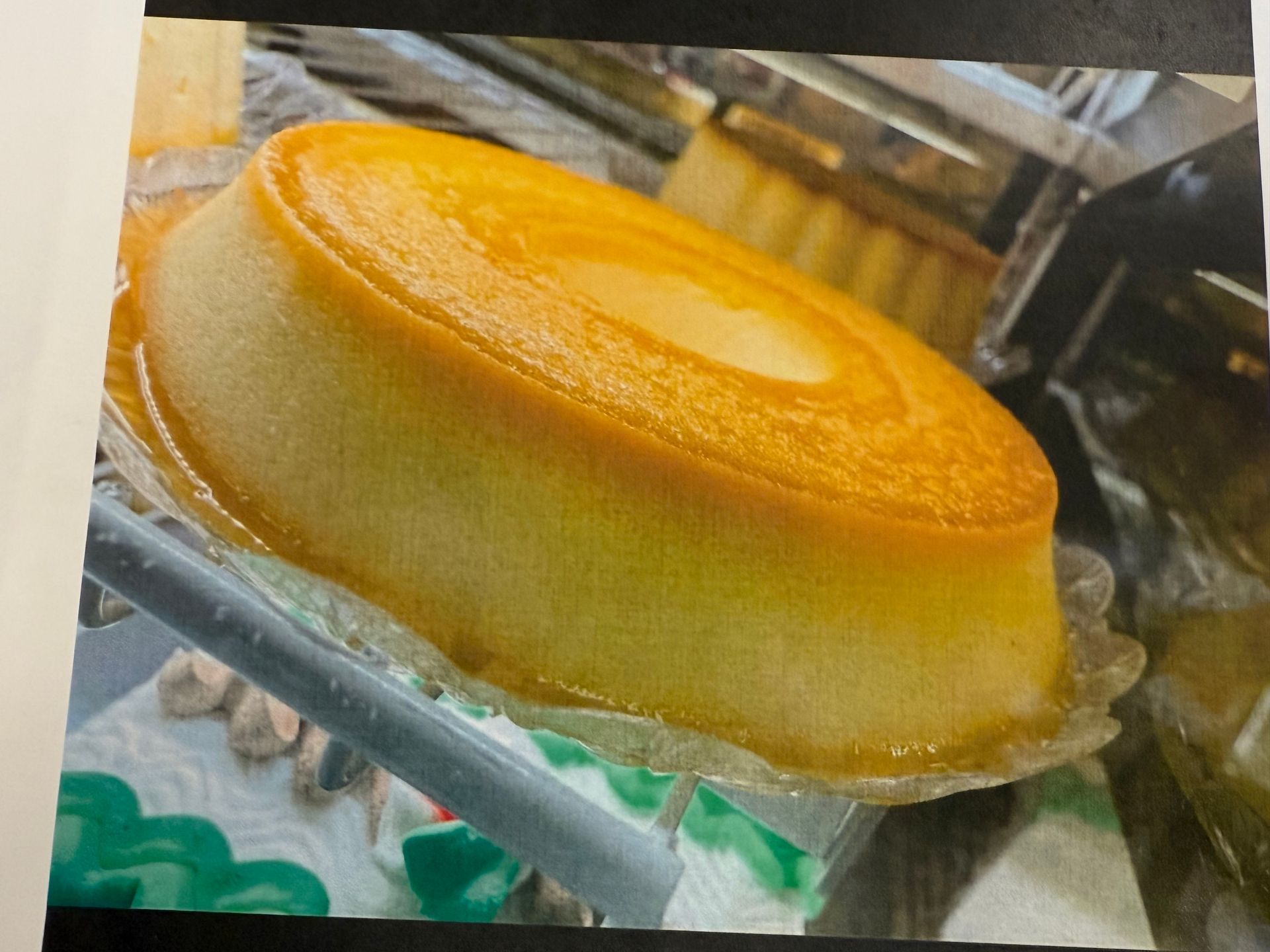 Flan in clear plastic container; caramel-colored top, pale yellow sides. Another flan in background.