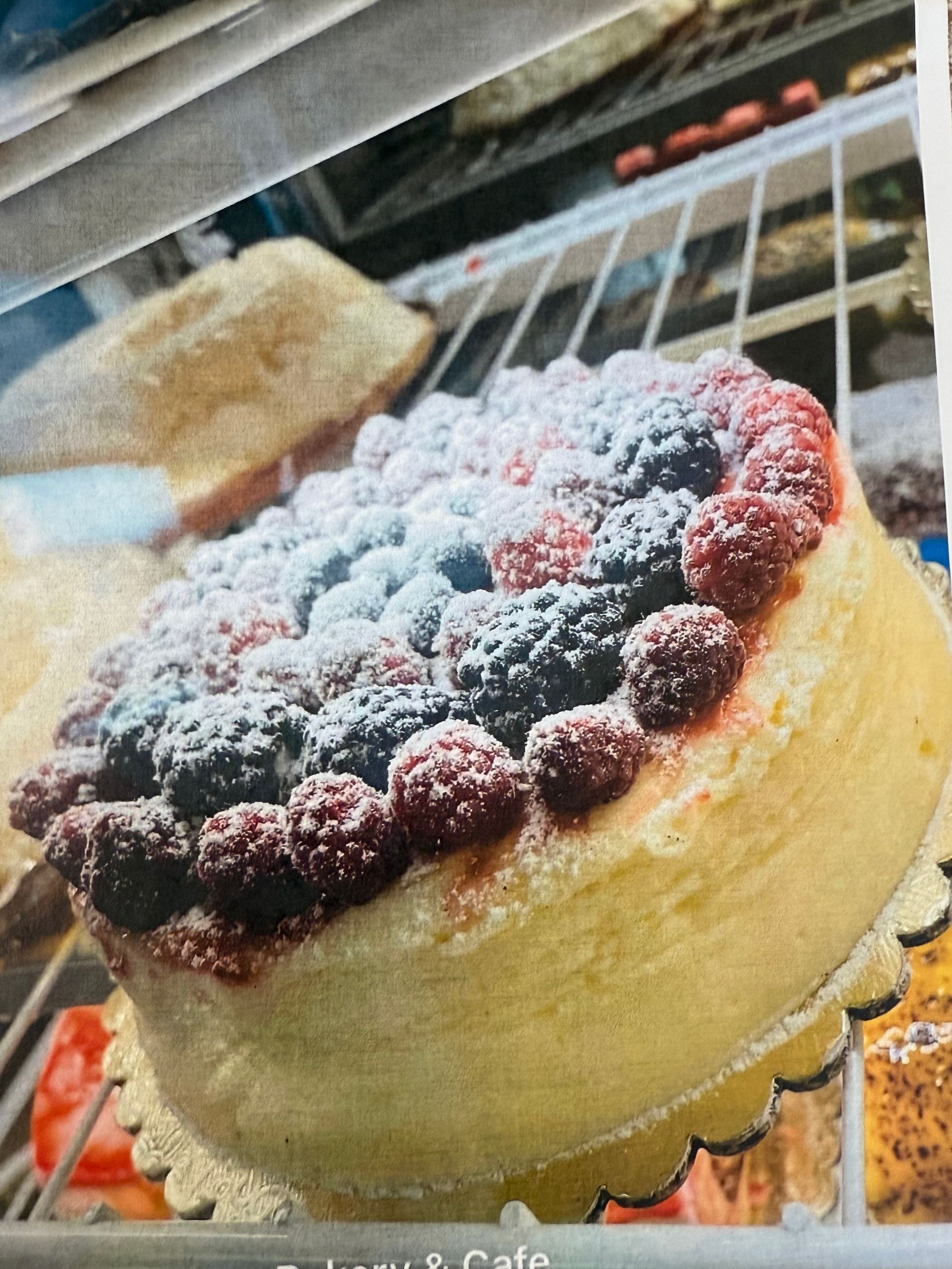 Cheesecake with raspberries and blackberries dusted with powdered sugar, displayed in a bakery case.