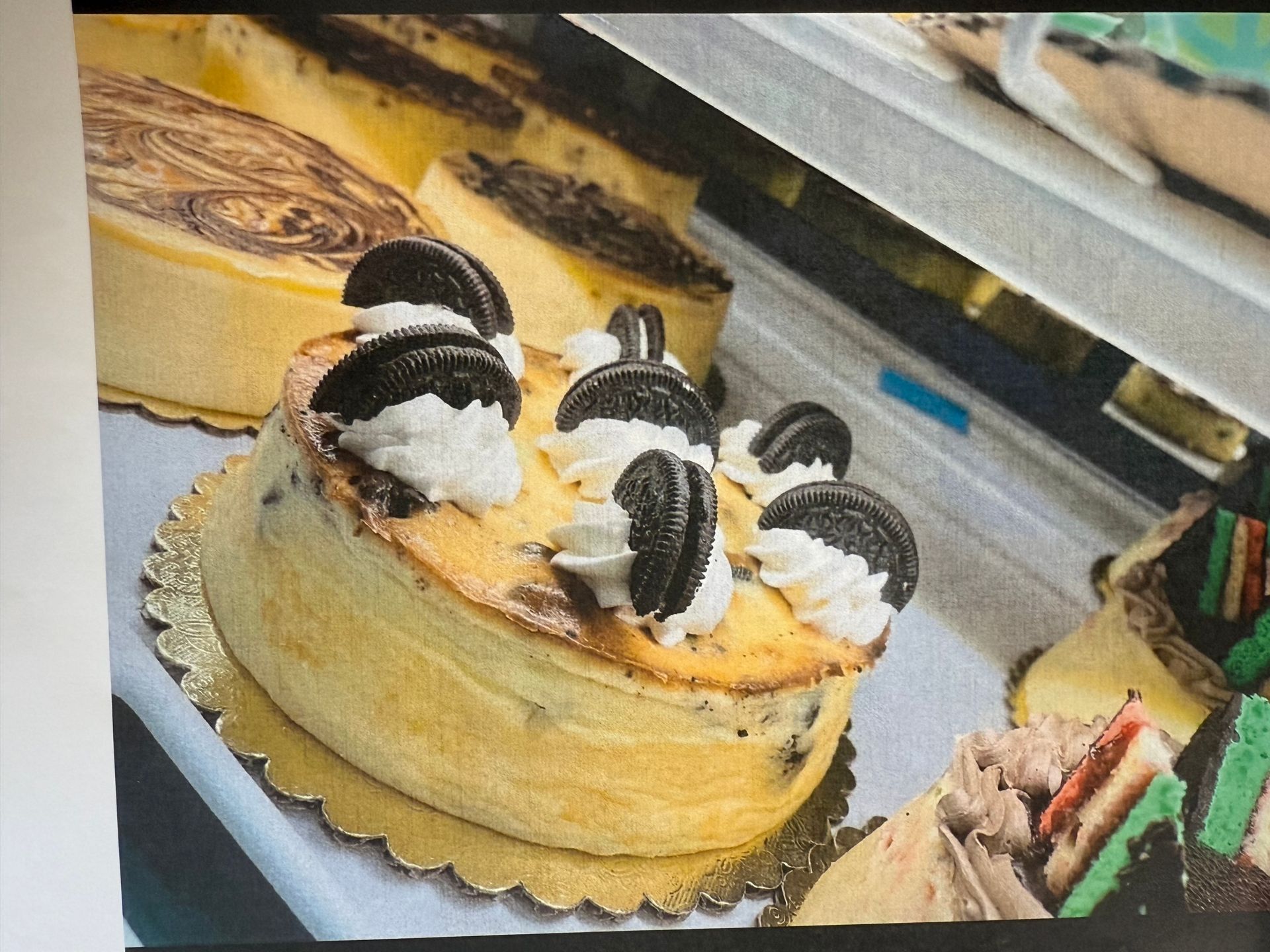 Oreo cheesecake on a gold-colored cake base in a display case with other desserts.