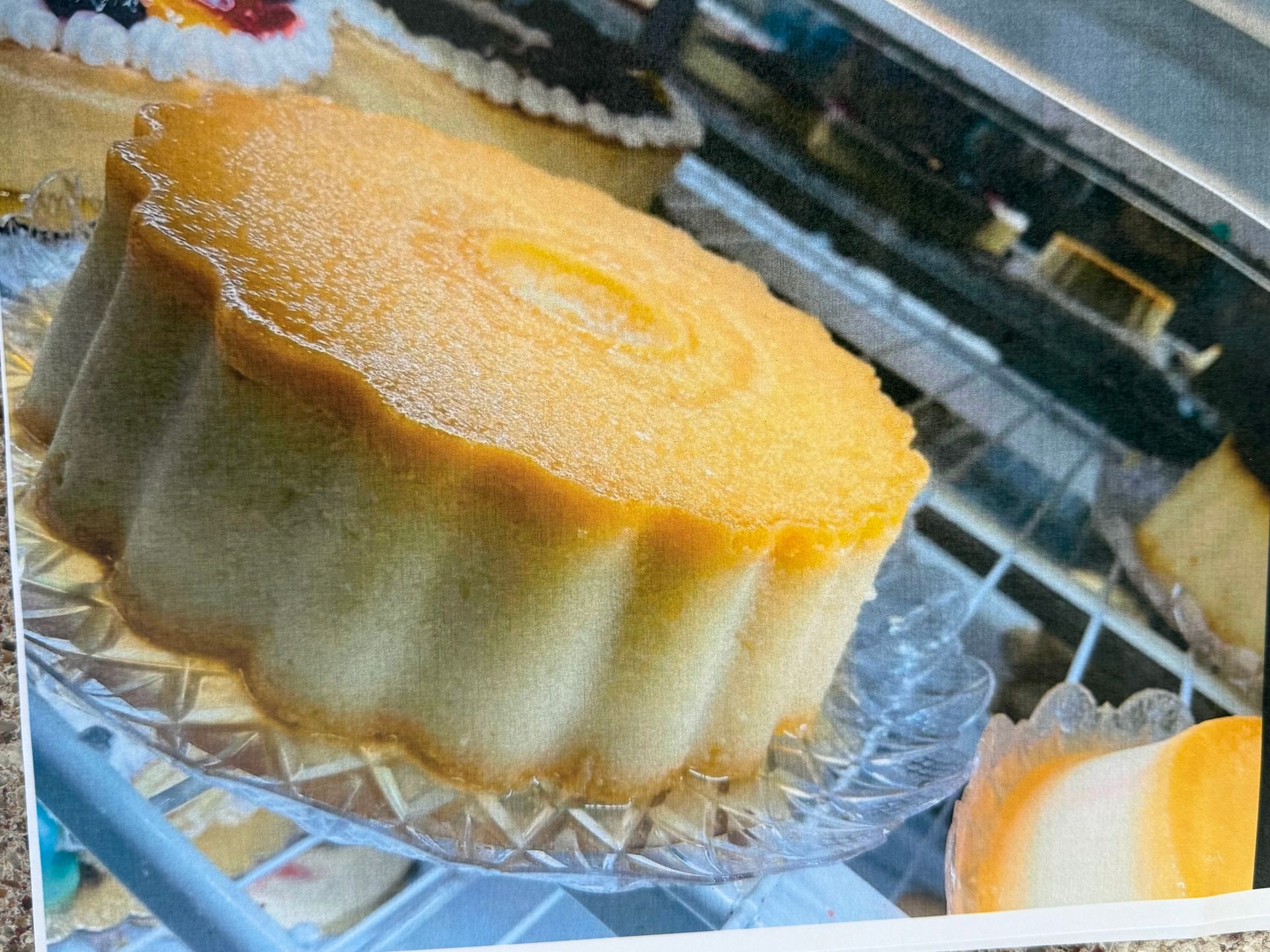 Yellow cake on a glass plate in a display case, light dusting of sugar.