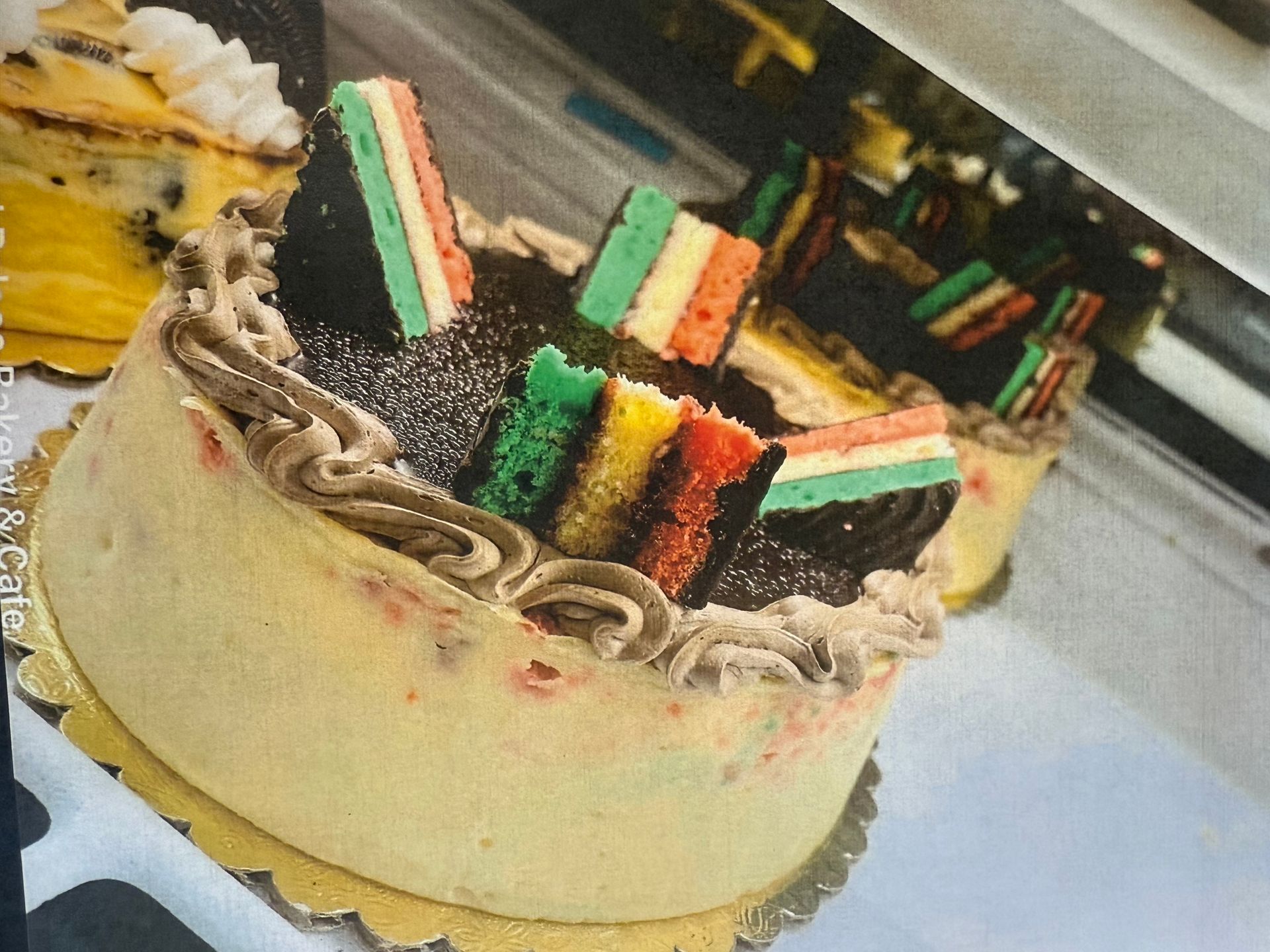 Round cake with colorful layers, chocolate topping, and frosting, on a gold plate.