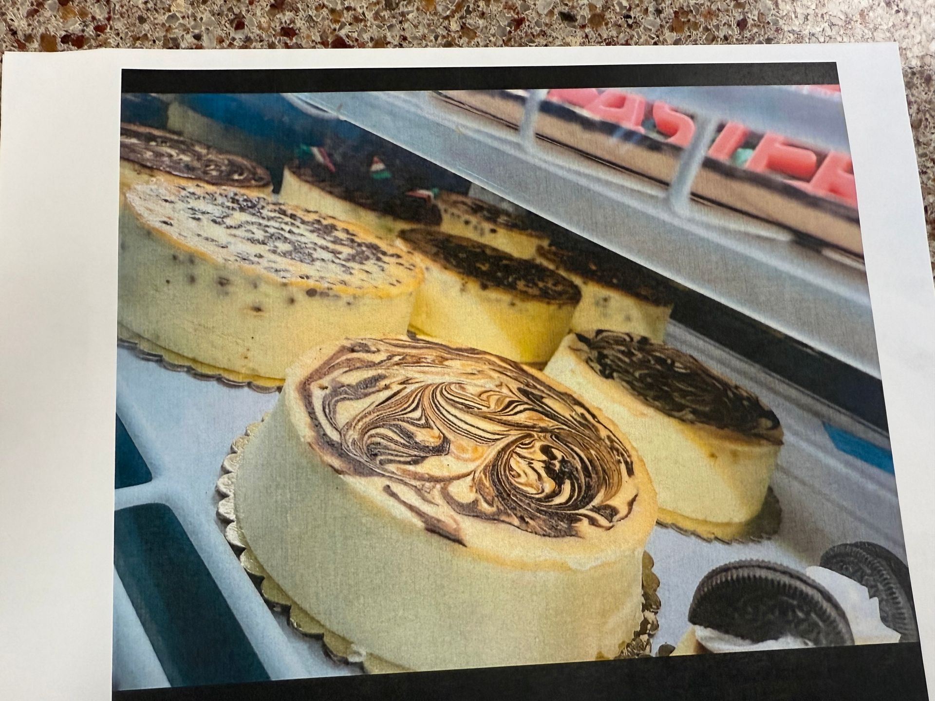 Cheesecakes in a glass display case, some with chocolate swirls and toppings.