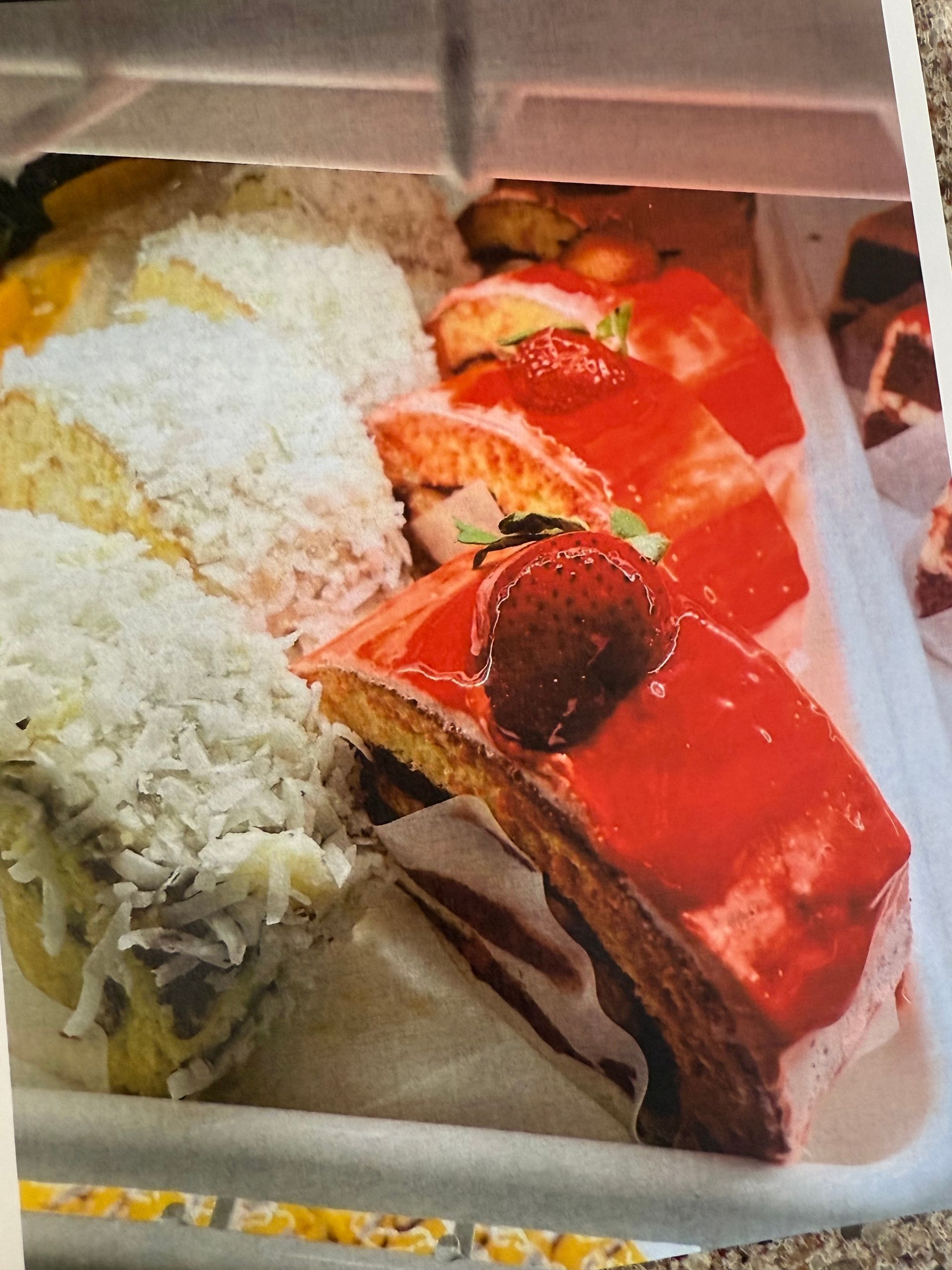Cake display: Coconut cake slices, strawberry-topped red-glazed cakes.