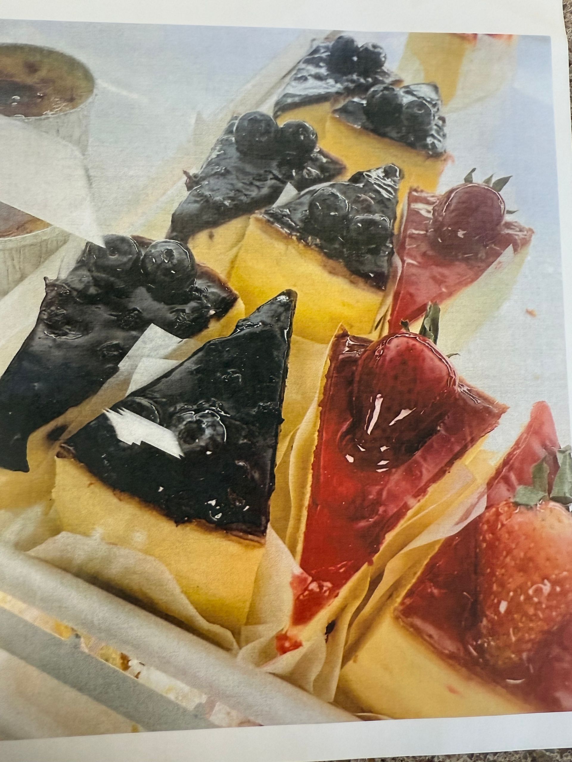 Cheesecake slices with blueberry and strawberry toppings, arranged on parchment paper.