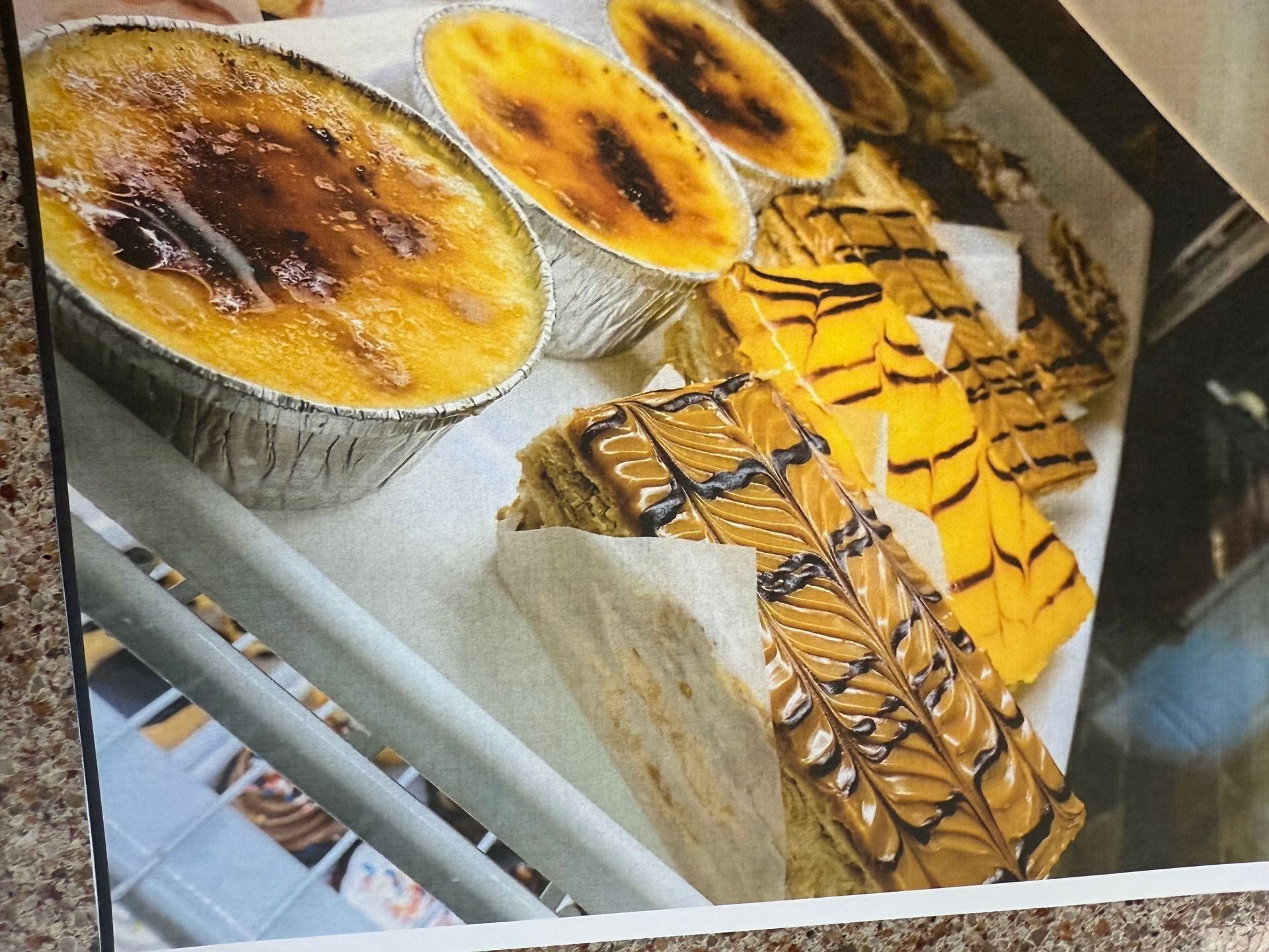 Assorted pastries: creme brûlée, layered cake with chocolate drizzle, and yellow glazed slices on display.