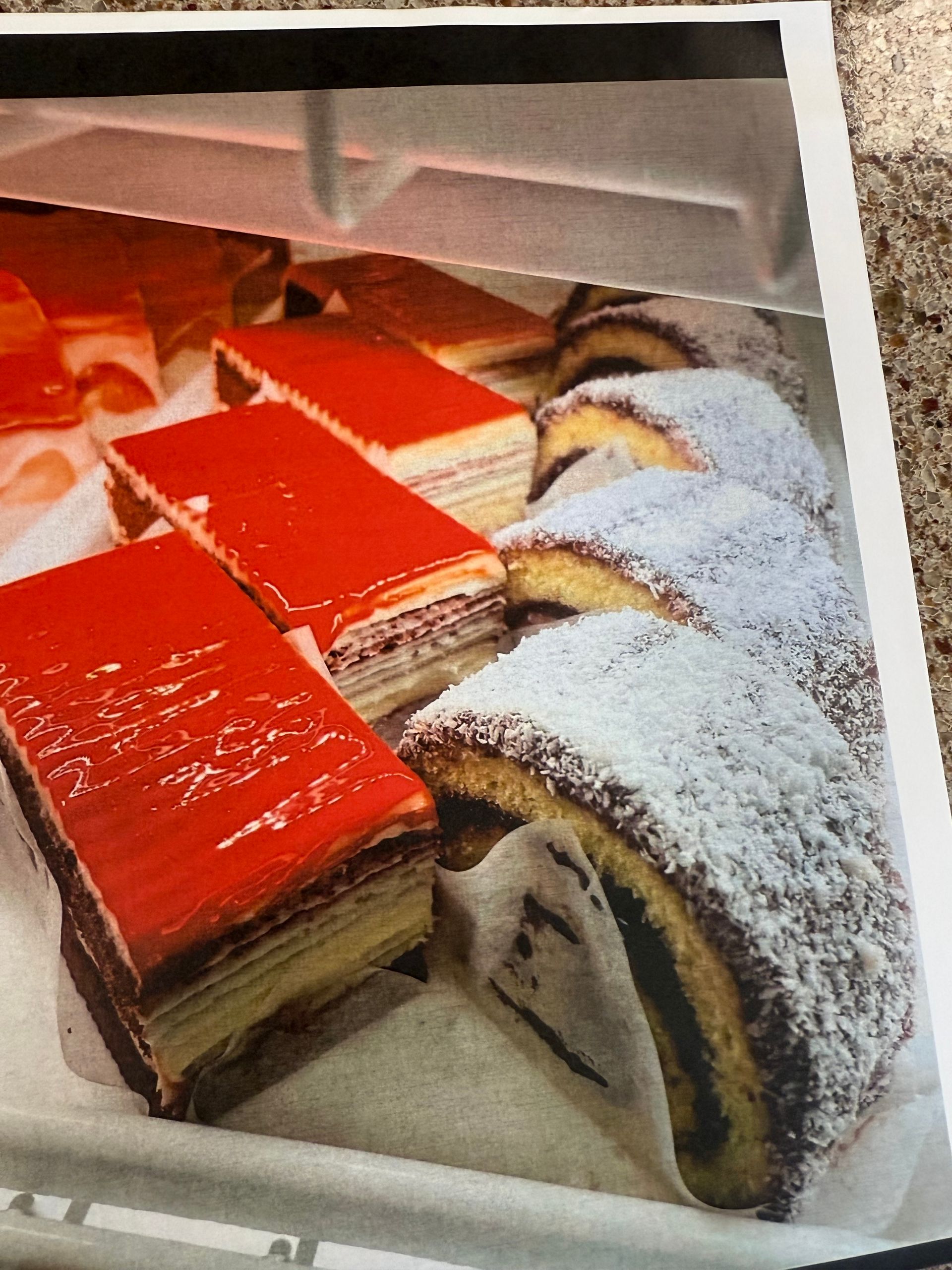 Display case with layered red-glazed pastries and powdered-sugar-dusted rolls.