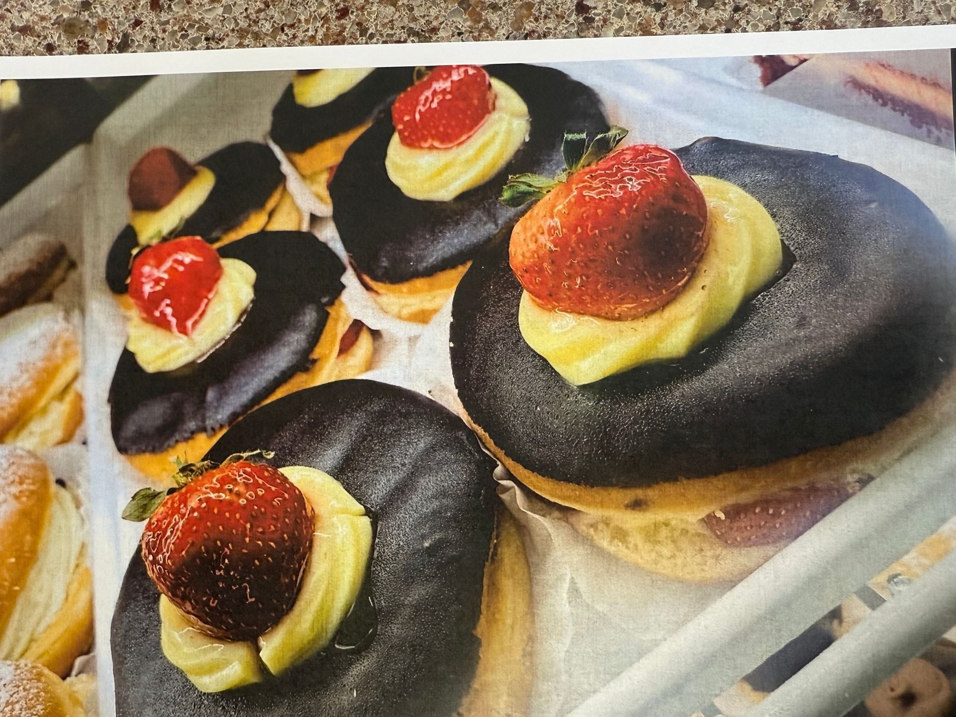 Donuts with dark chocolate glaze, custard, and strawberries, in a bakery display case.