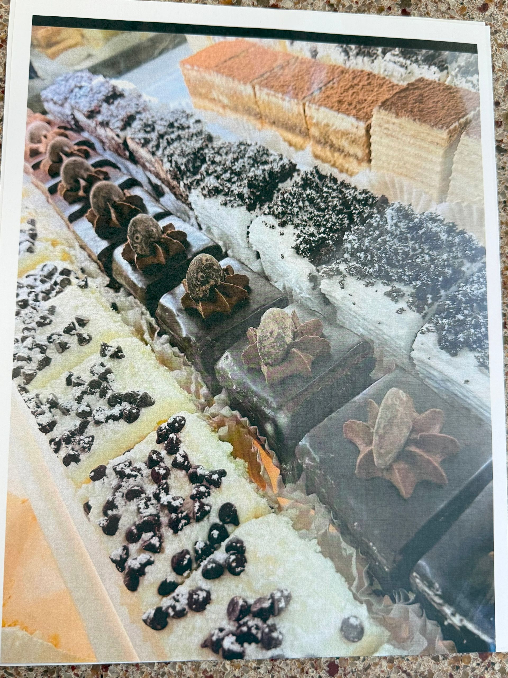 Display case with assorted pastries, including chocolate, cream, and layered cakes, arranged on a tray.