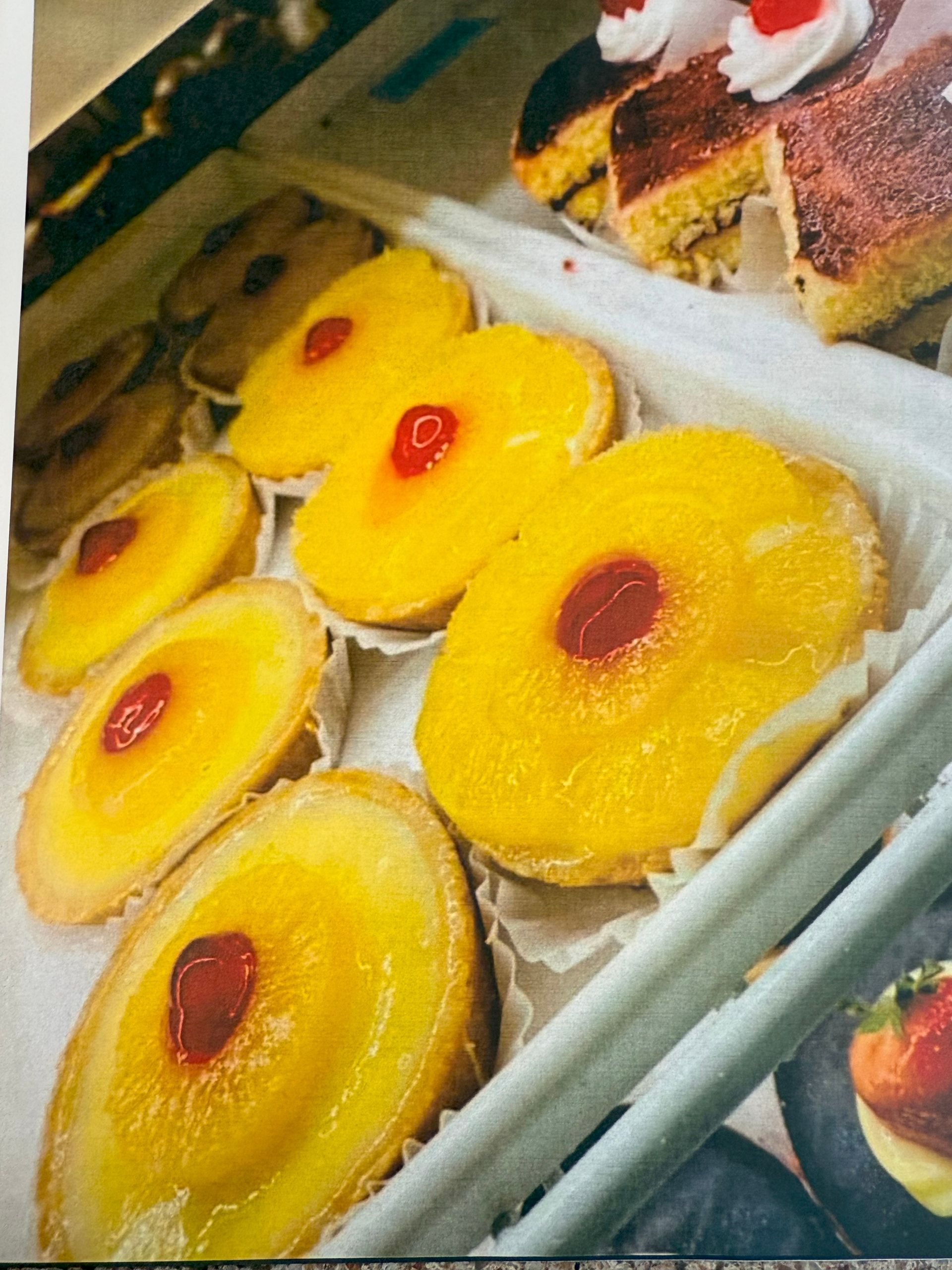 Pastries in a display case; yellow and round with cherry topping.