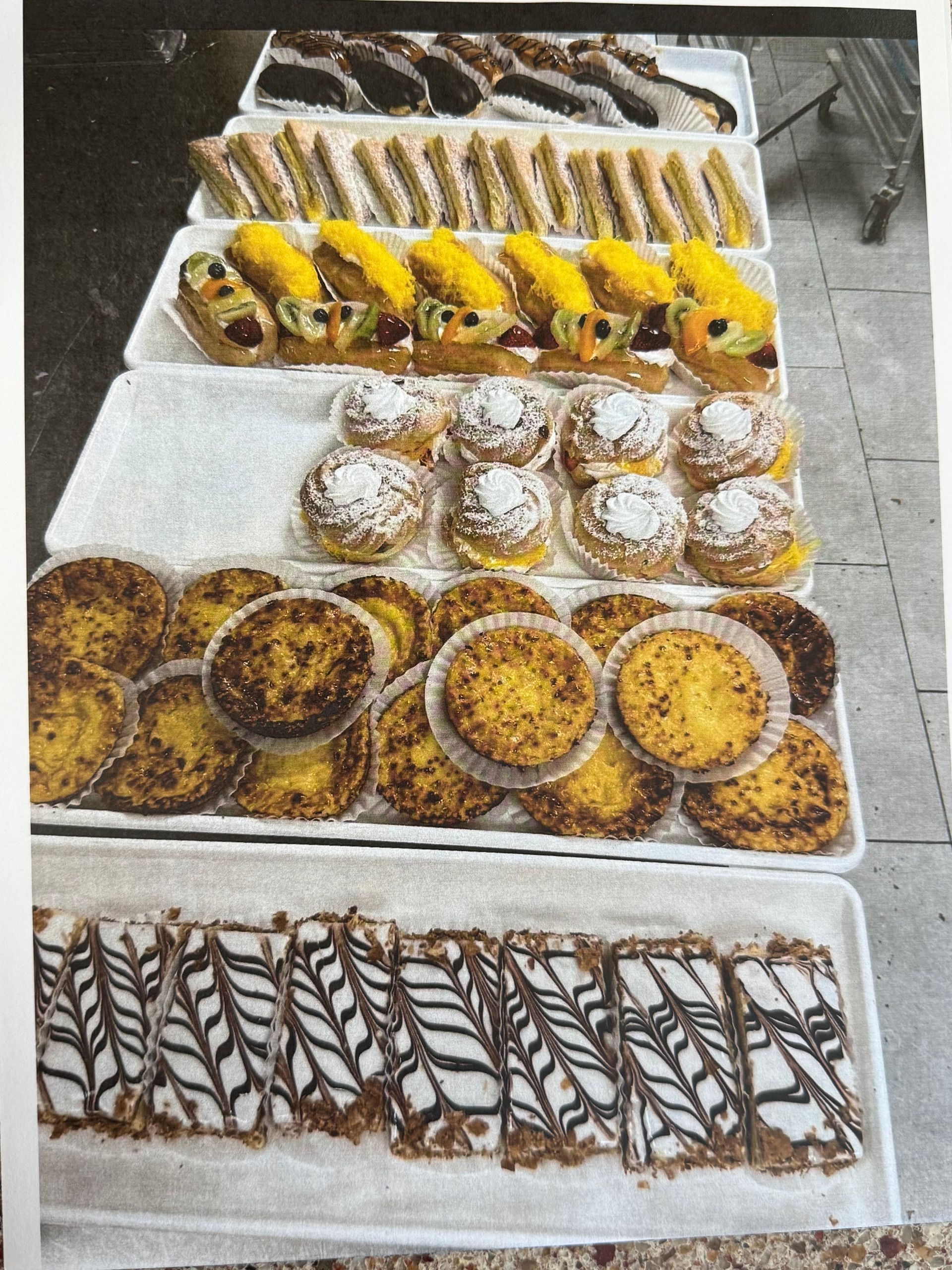 Various pastries displayed on white trays, including sandwiches, custard tarts, and cream puffs.