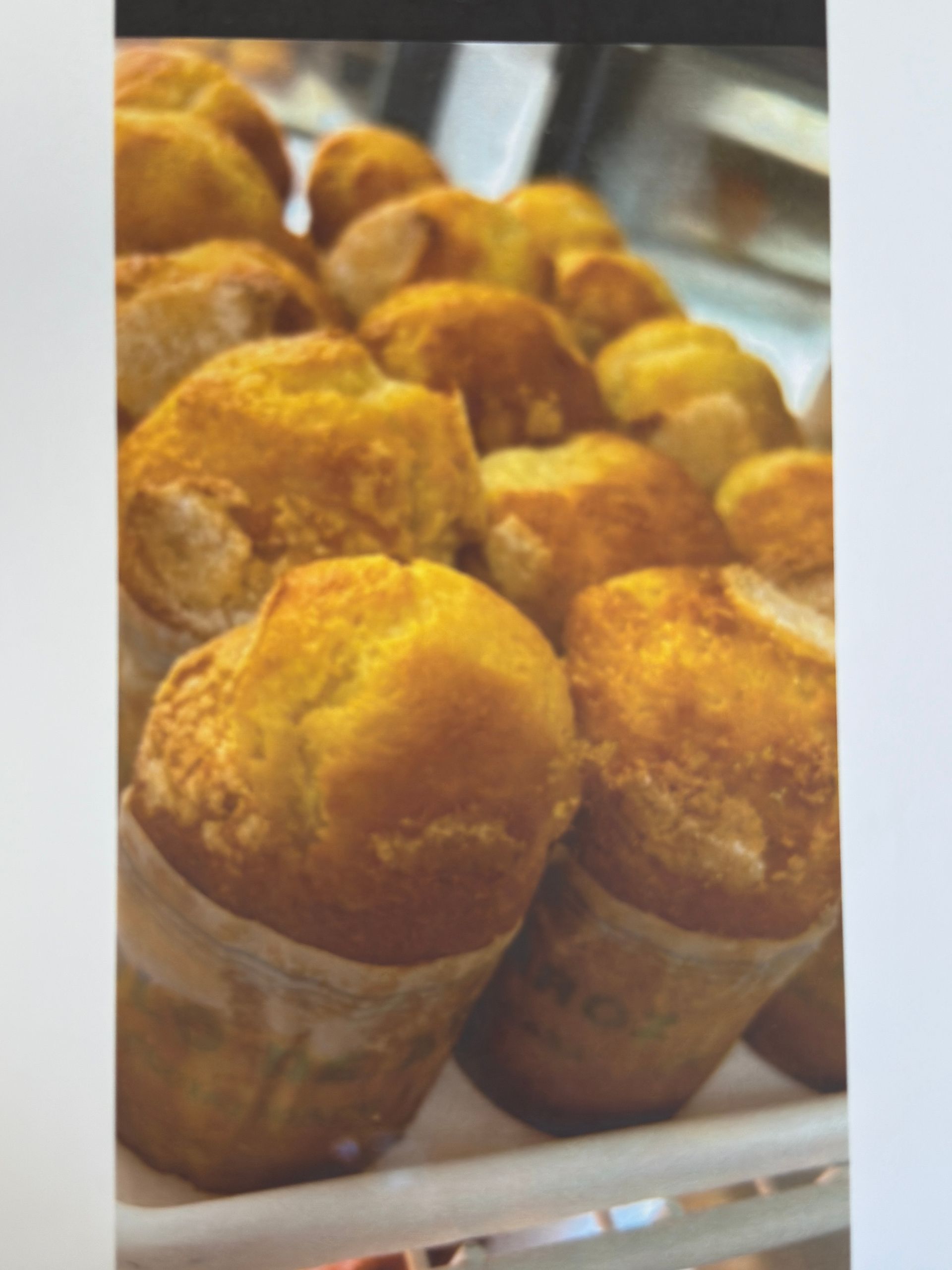 Rows of golden-brown, muffin-shaped pastries in a display case.