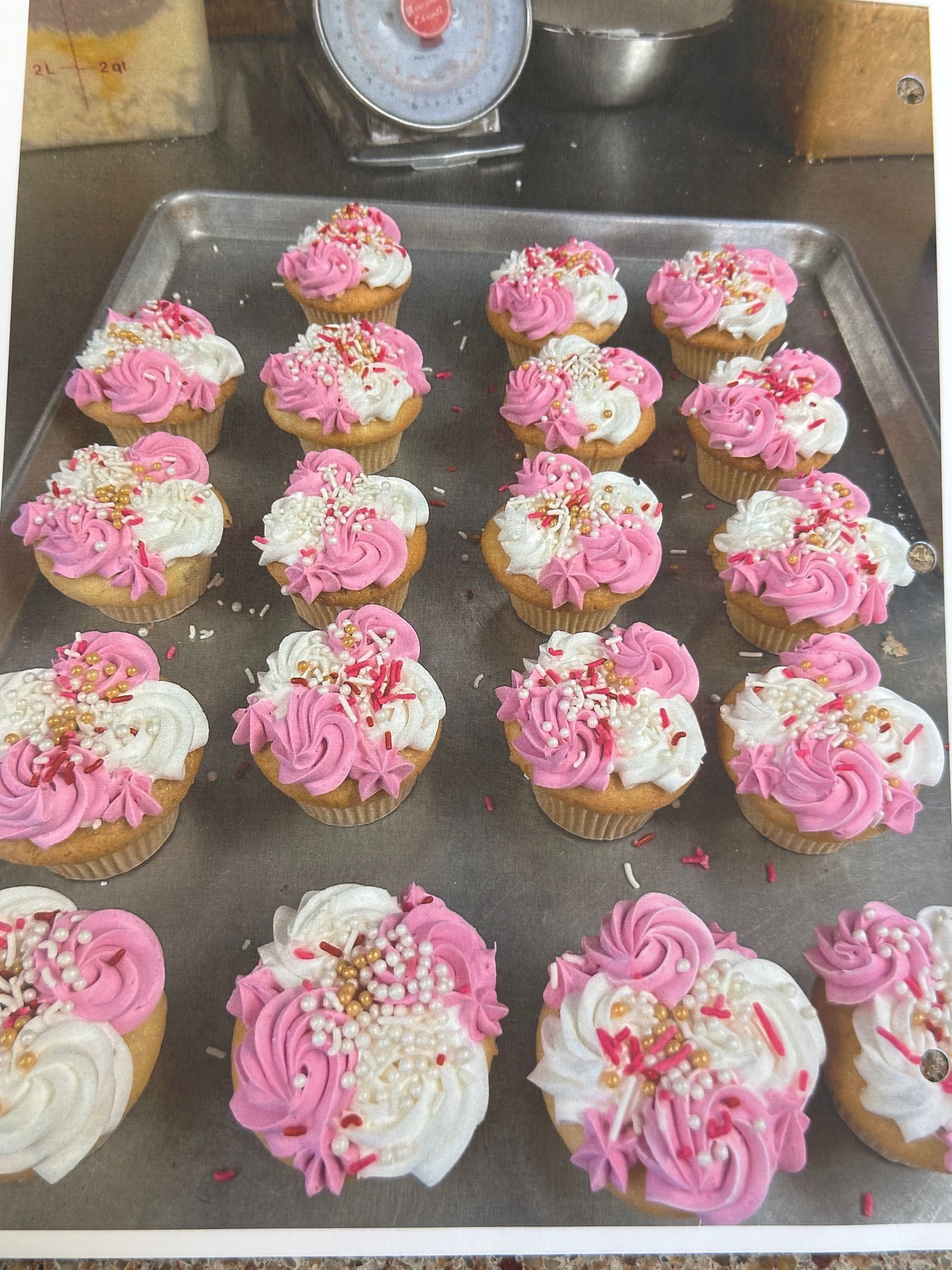 Tray of cupcakes with pink and white frosting, sprinkled with edible glitter.