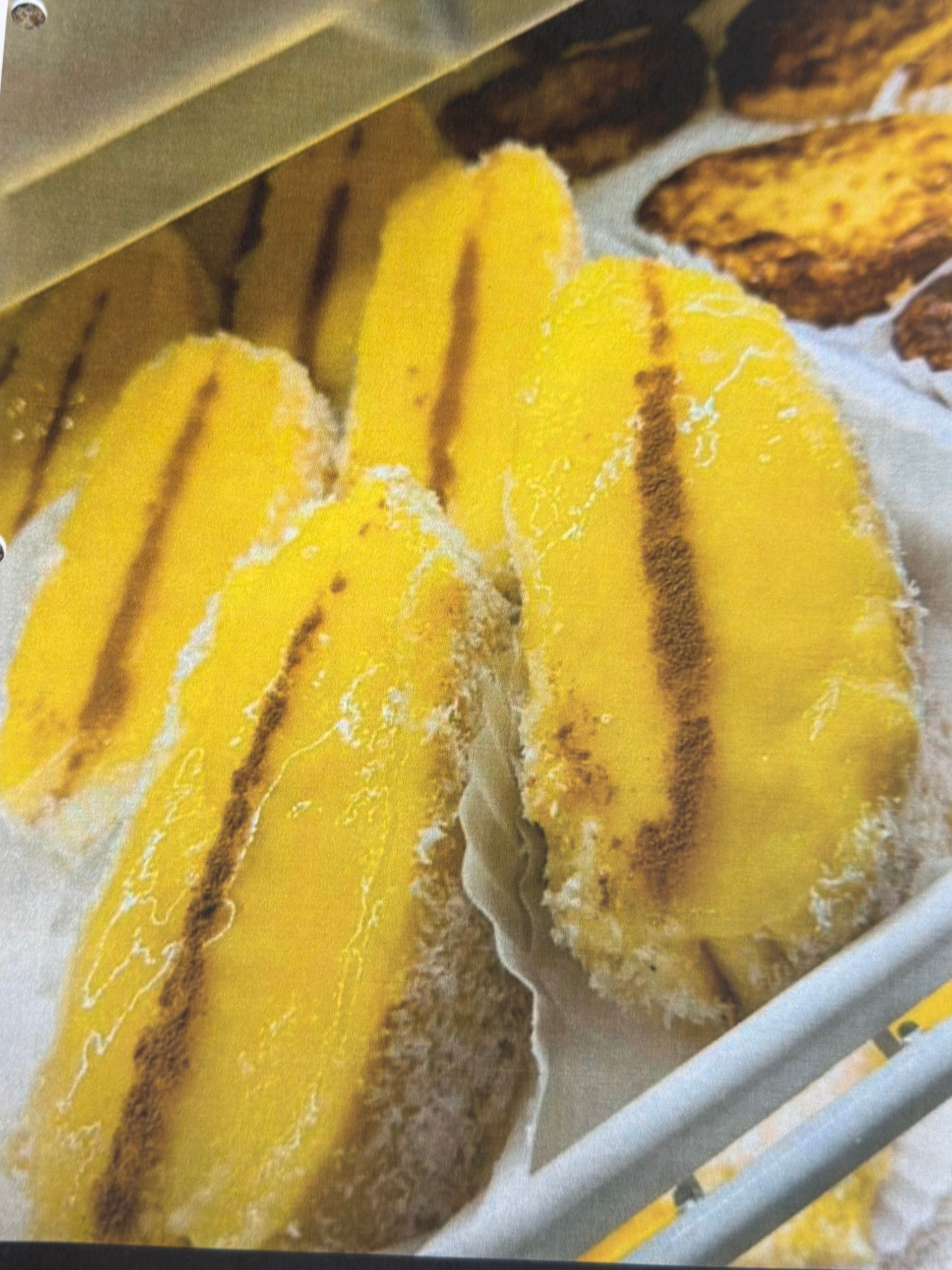 Yellow pastries with dark lines on a tray in a display case.