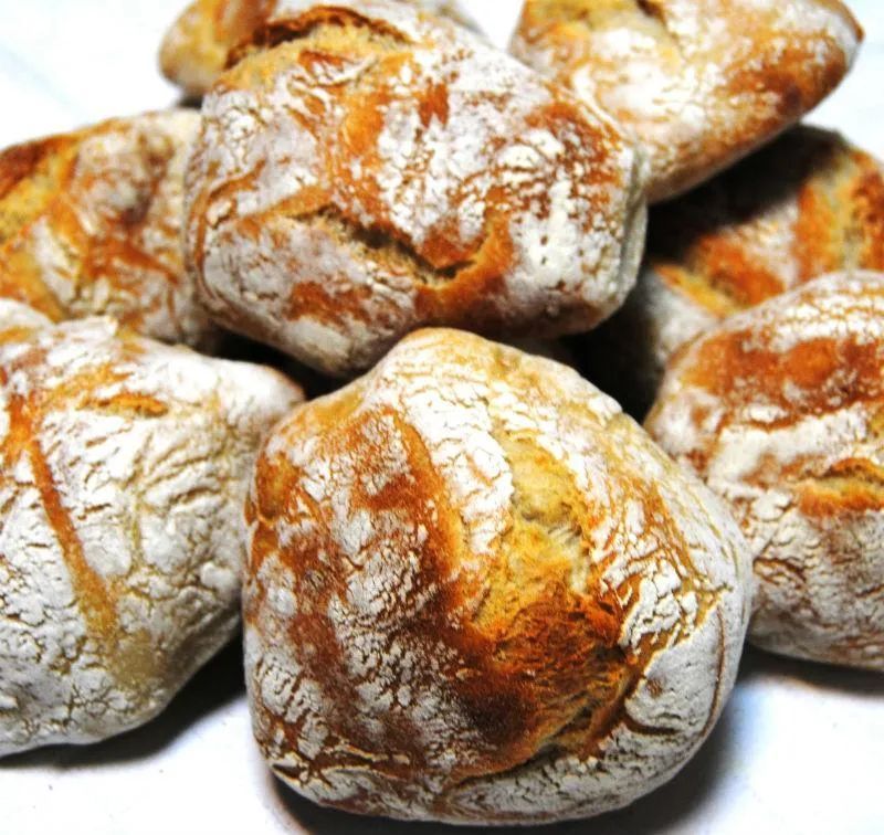 Pile of rustic, golden-brown bread rolls dusted with white flour.